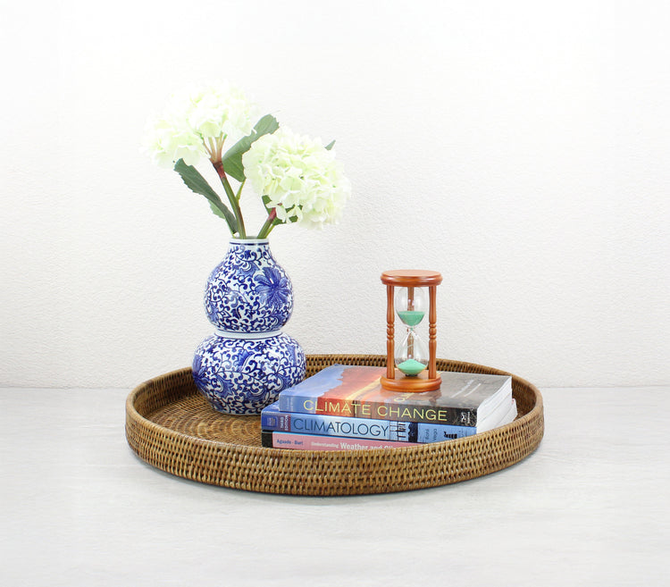 ECO HANDCRAFT extra-large round rattan tray in honey brown with vase, books, and hourglass styled on table