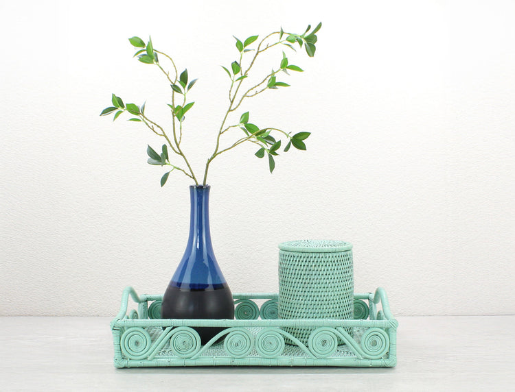 ECO HANDCRAFT swirly sage leaf green rectangle rattan tray with blue vase and canister styled on a neutral tabletop for home decor.