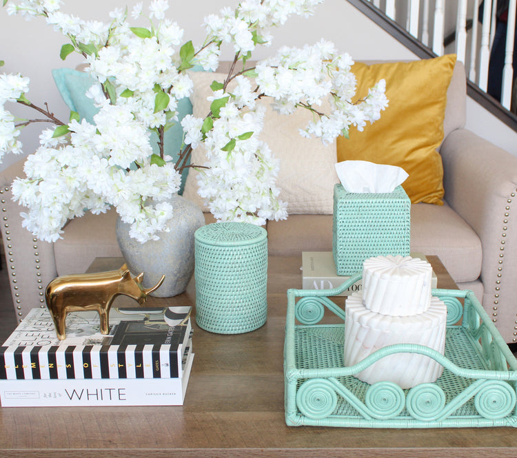 Sage green rattan decor on styled coffee table with cherry blossoms, candles, and gold rhino in cozy modern living room.