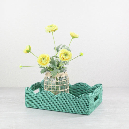 Turquoise scalloped rattan tray with a glass flower vase and yellow blooms, styled for spring home or table decor.