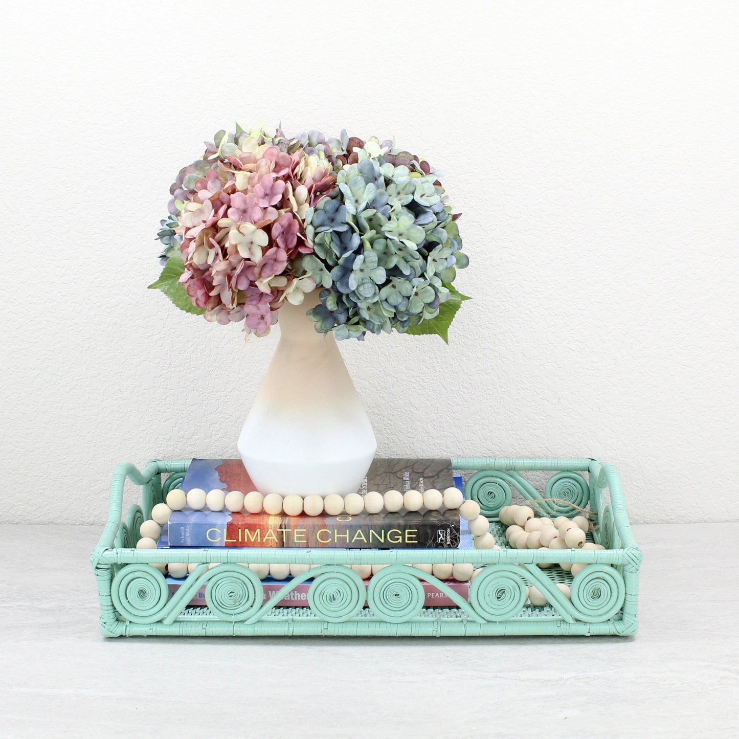 Sage Leaf Green rectangular rattan tray with swirl edge design, styled with hydrangeas in a white vase, books, and wooden bead garland for modern décor.