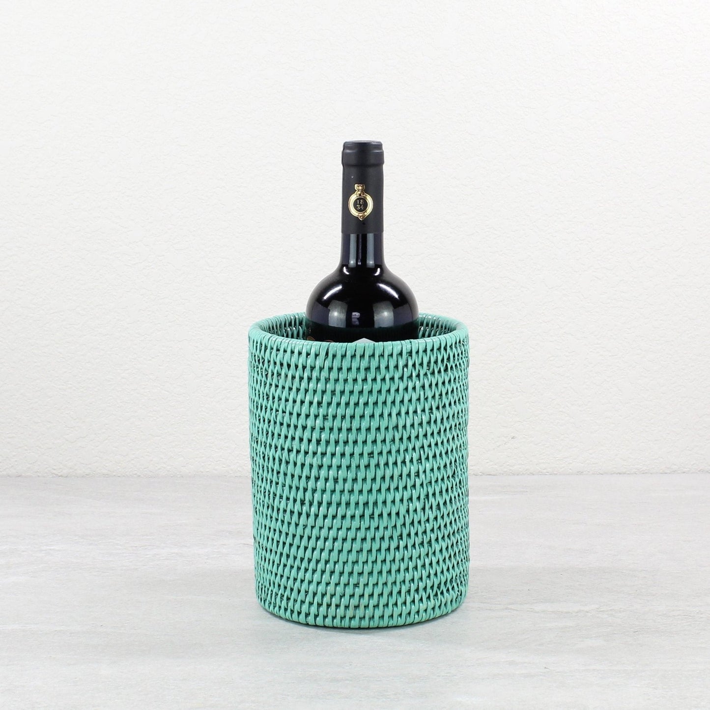 Eco Handcraft Turquoise handwoven rattan wine bottle holder with a black wine bottle inside, styled on a gray table.