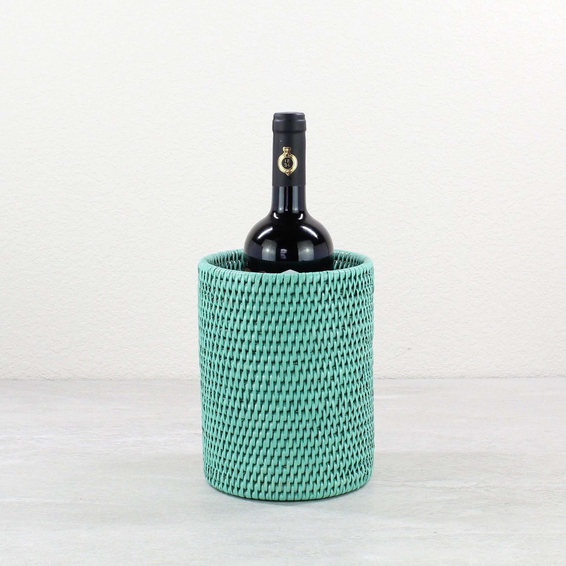 Eco Handcraft Turquoise handwoven rattan wine bottle holder with a black wine bottle inside, styled on a gray table.