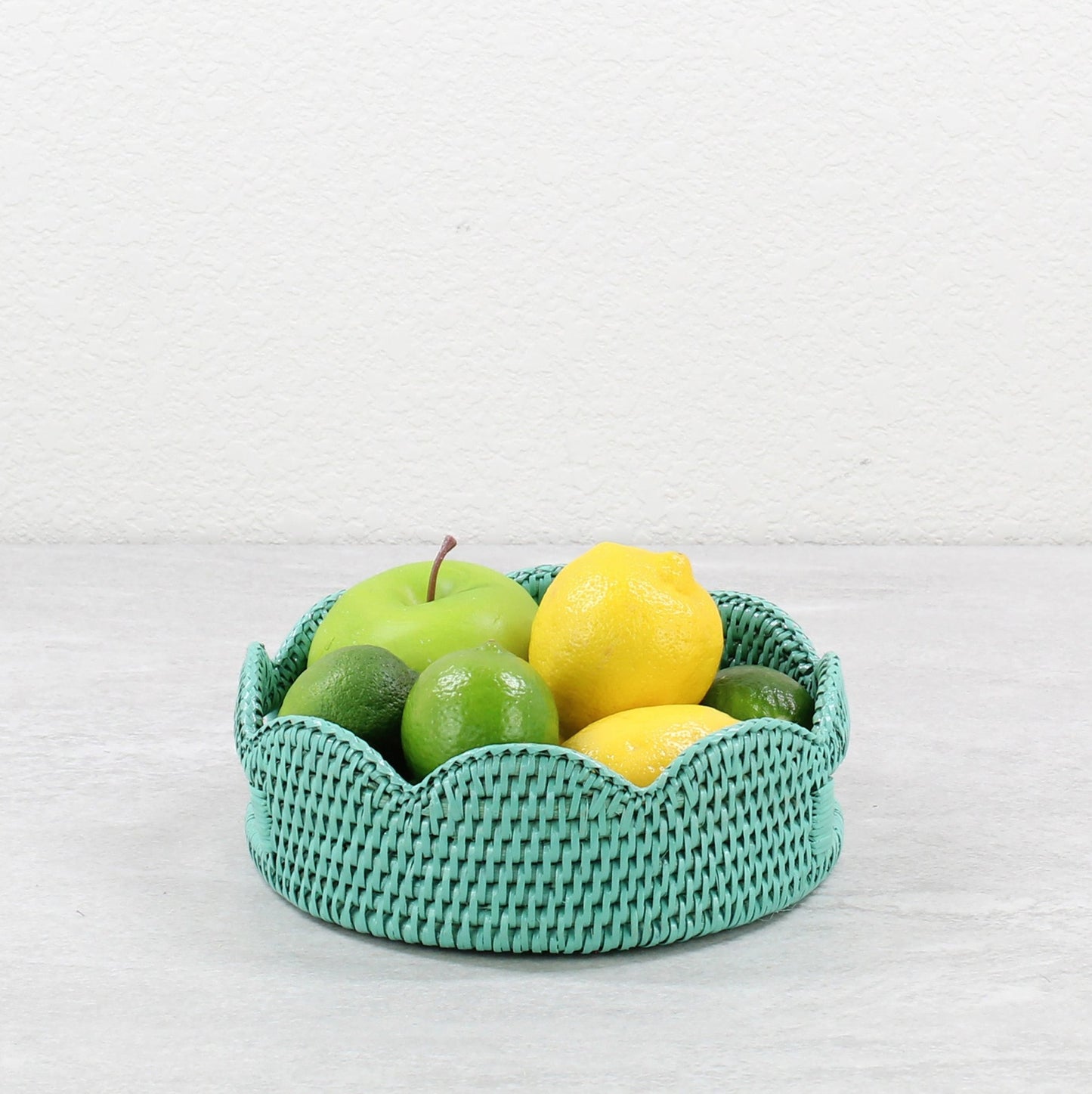 Eco-friendly round turquoise rattan fruit basket with lemons, limes, and apple—perfect for natural kitchen styling.