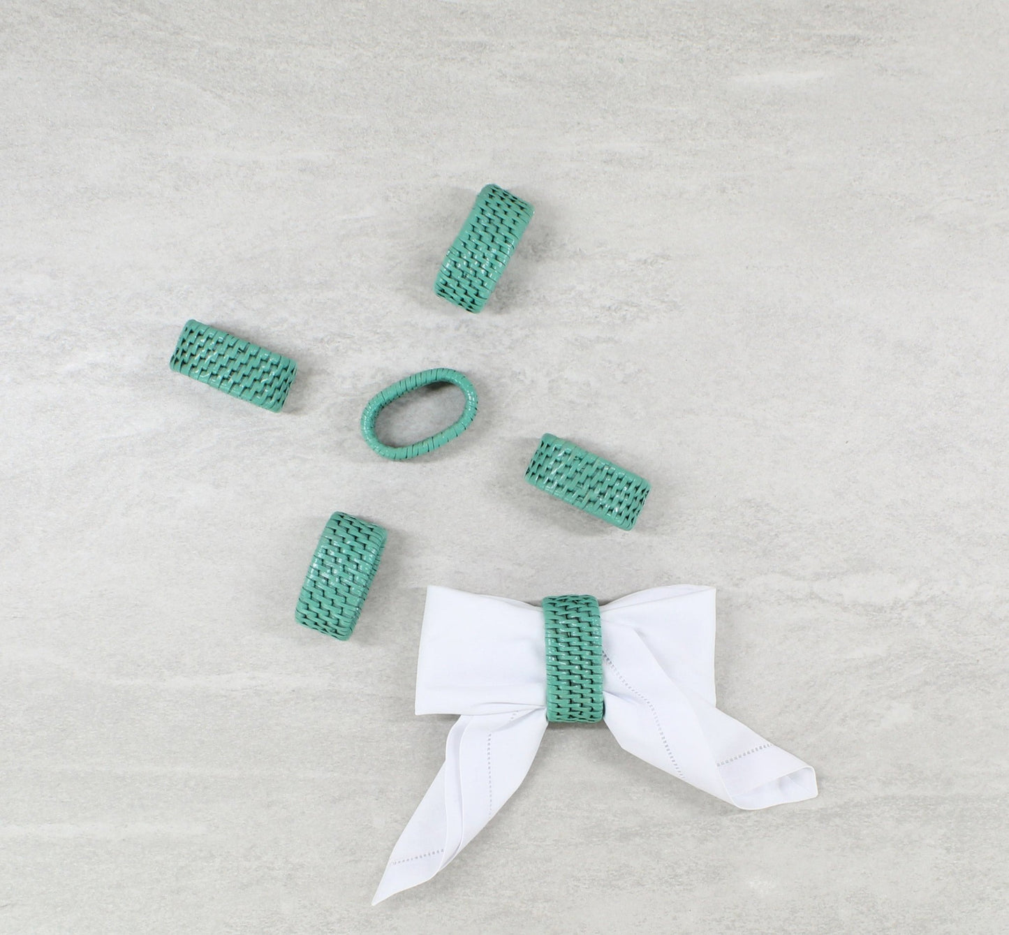 Set of turquoise woven rattan napkin rings with one styled holding a white napkin in a oval shape.