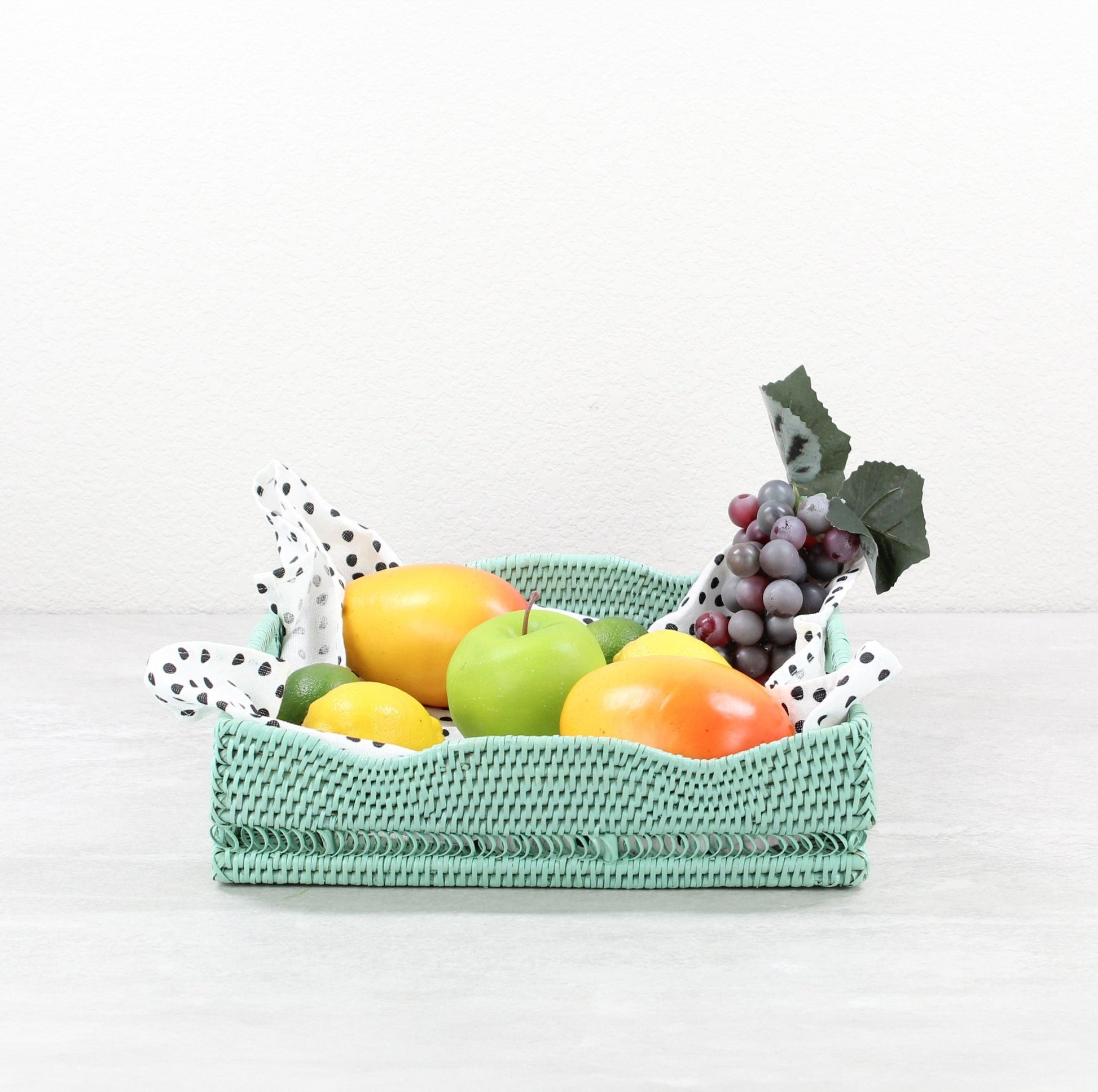 ECO HANDCRAFT sage green rectangular rattan fruit tray with scalloped edge, styled with lemons, apples, and grapes