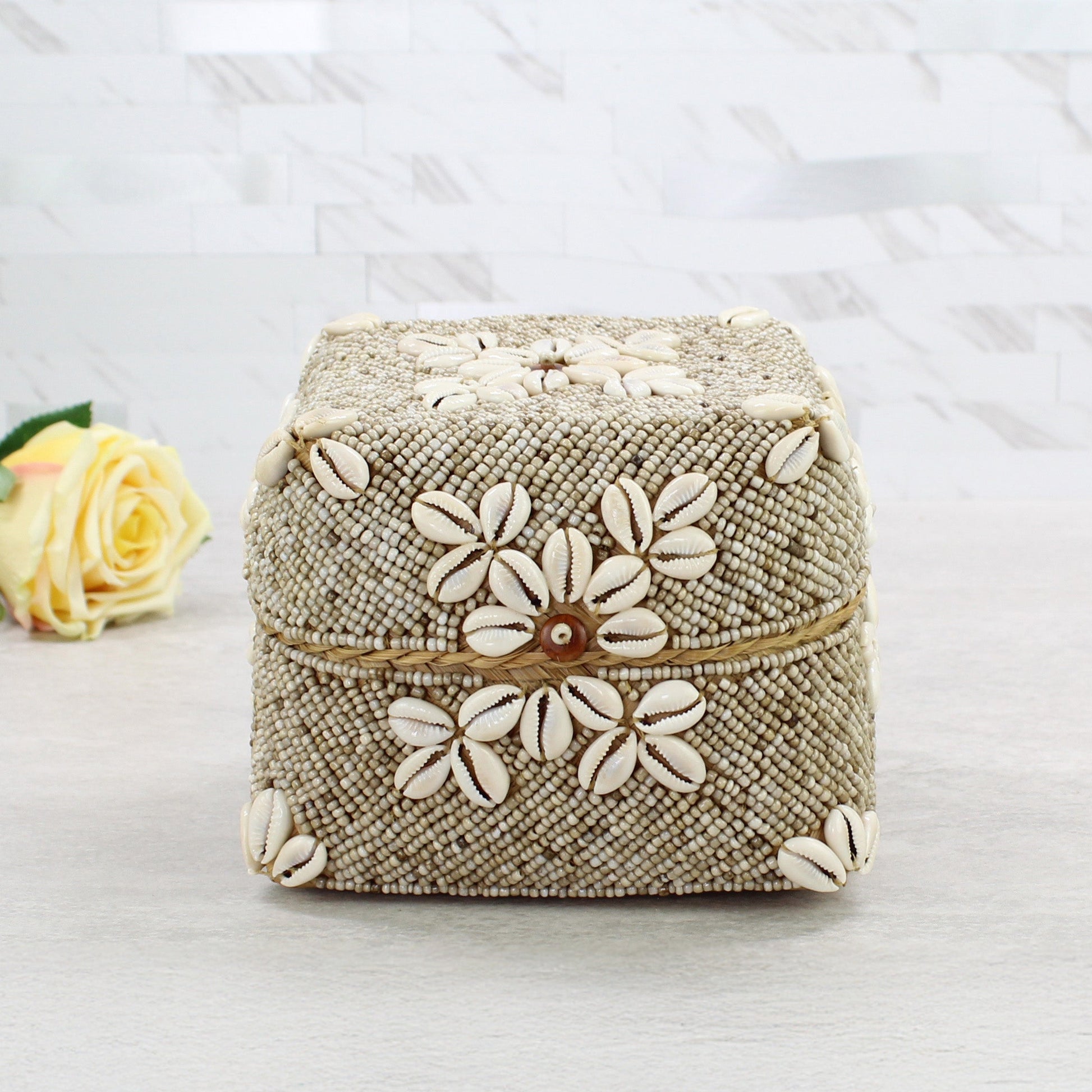 Medium handmade beige beaded storage box with delicate cowrie shell floral accents, placed beside soft yellow roses for styling inspiration.