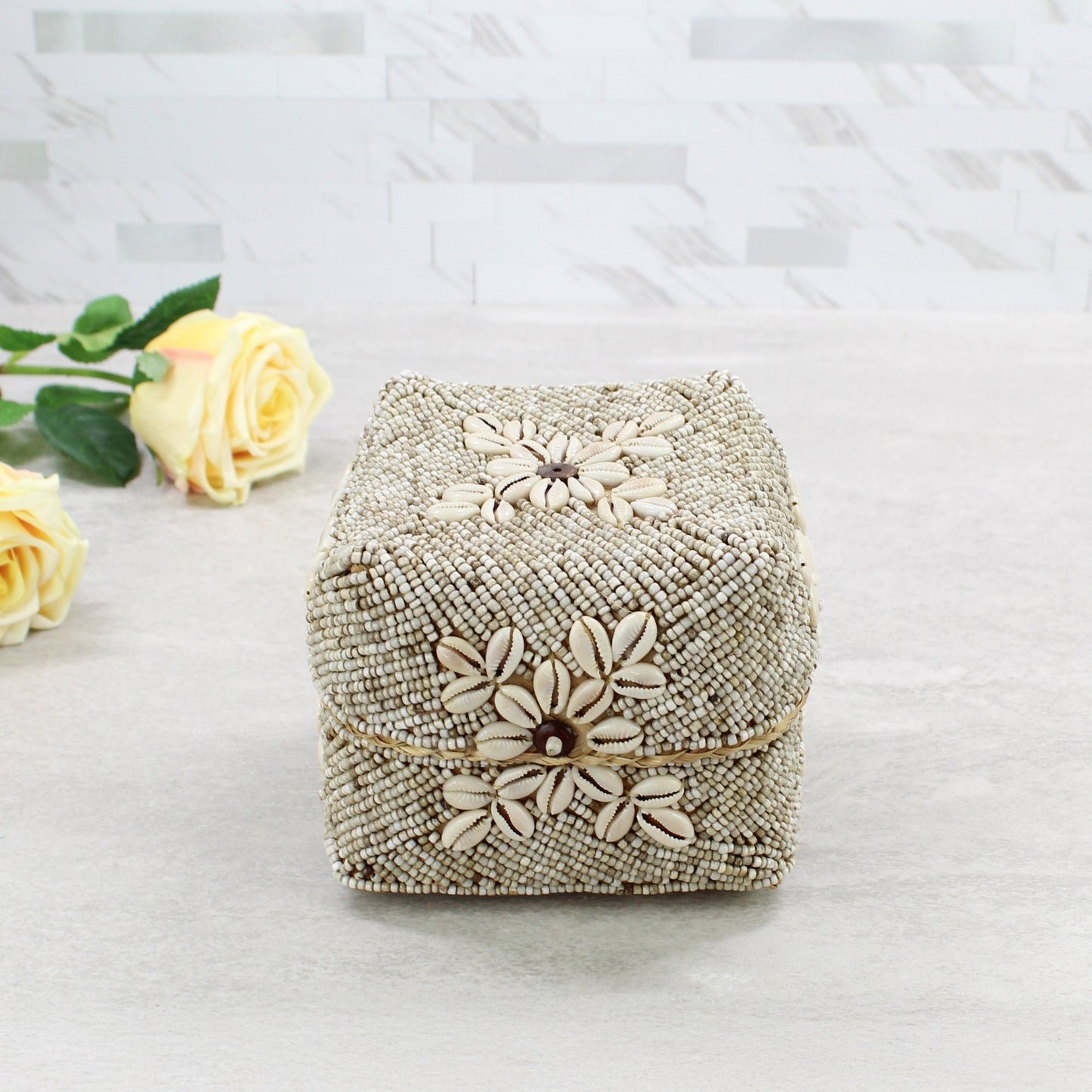 Top view of beige beaded storage box decorated with natural cowrie shells and central flower motif in coastal boho décor style.