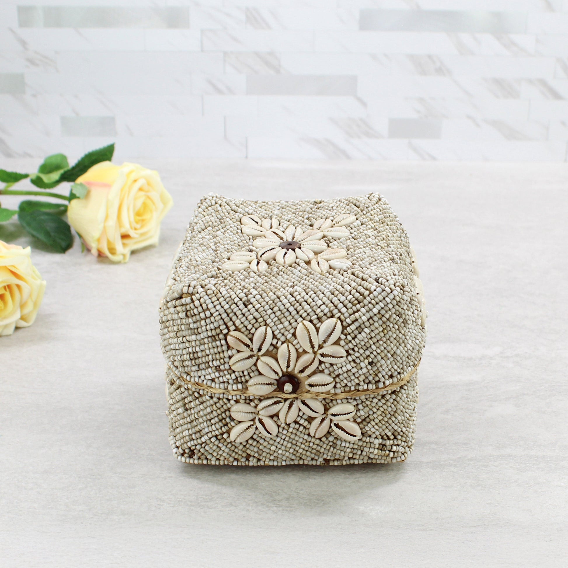 Top view of beige beaded storage box decorated with natural cowrie shells and central flower motif in coastal boho décor style.