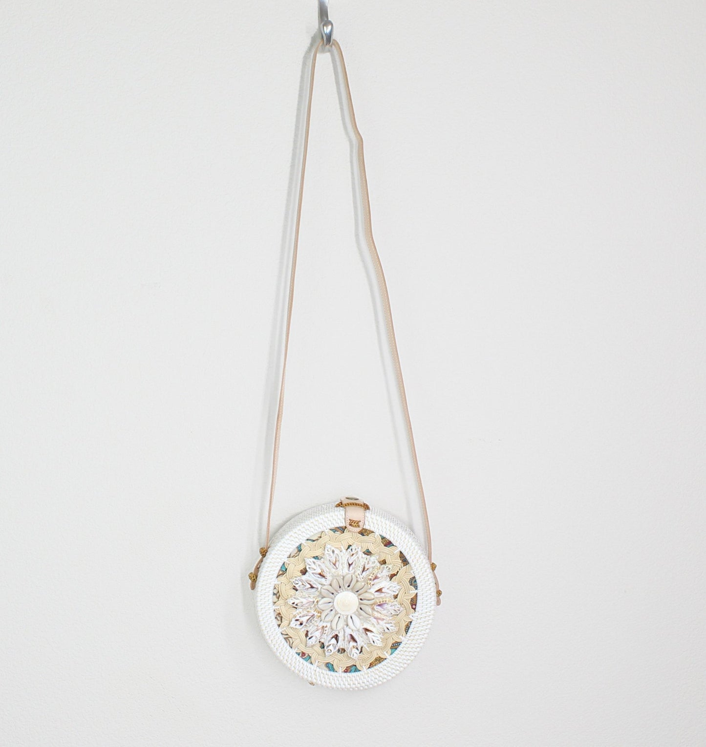 Seashell-decorated Bali rattan crossbody bag hanging on hook, blending coastal elegance with handcrafted design.
