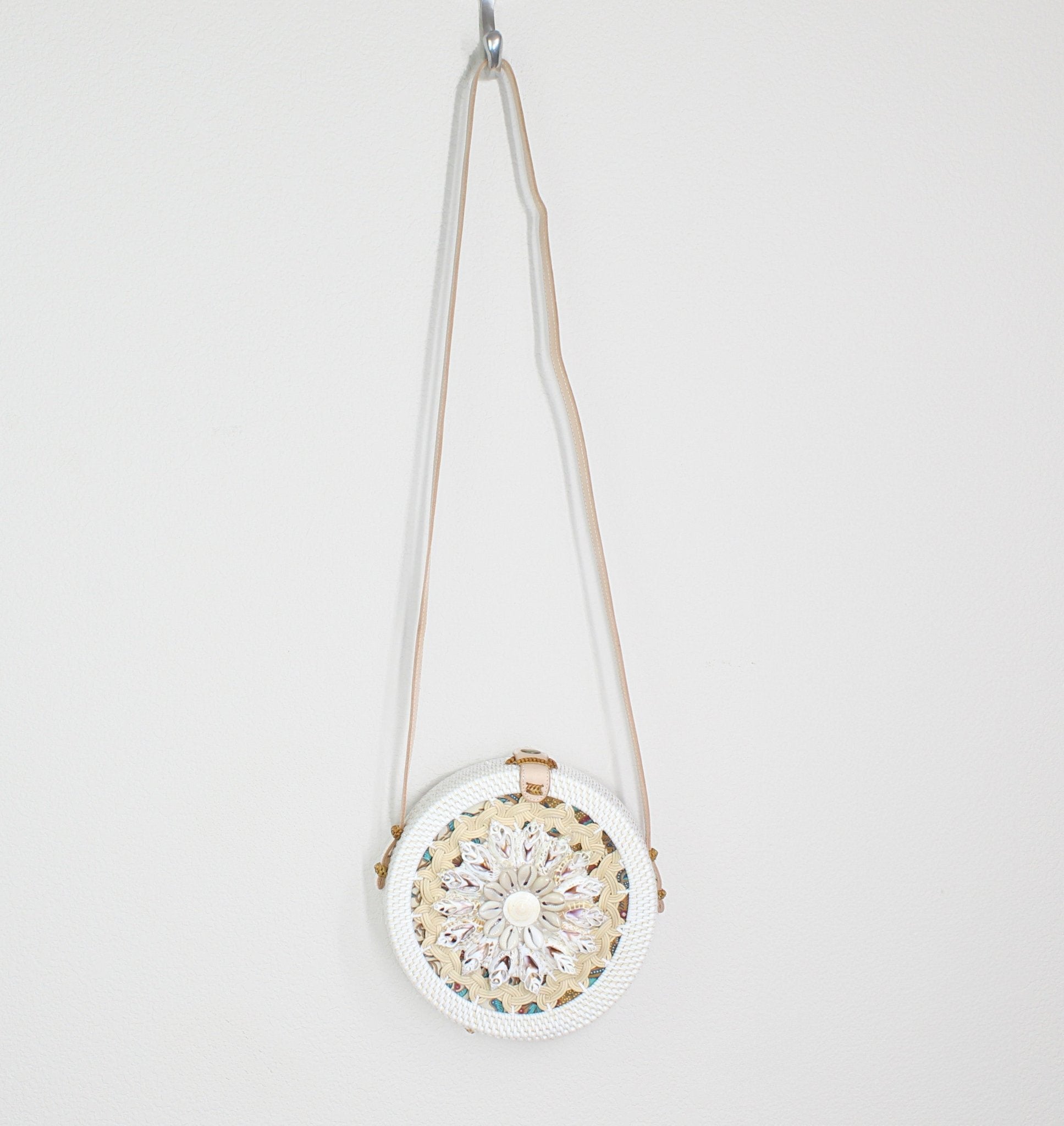 Seashell-decorated Bali rattan crossbody bag hanging on hook, blending coastal elegance with handcrafted design.