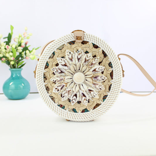 Bali-style round rattan crossbody bag with seashell flower design, placed on a table