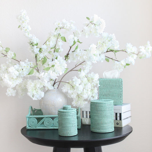 Eco Handcraft sage green rattan bathroom set on black table with white cherry blossoms in a vase