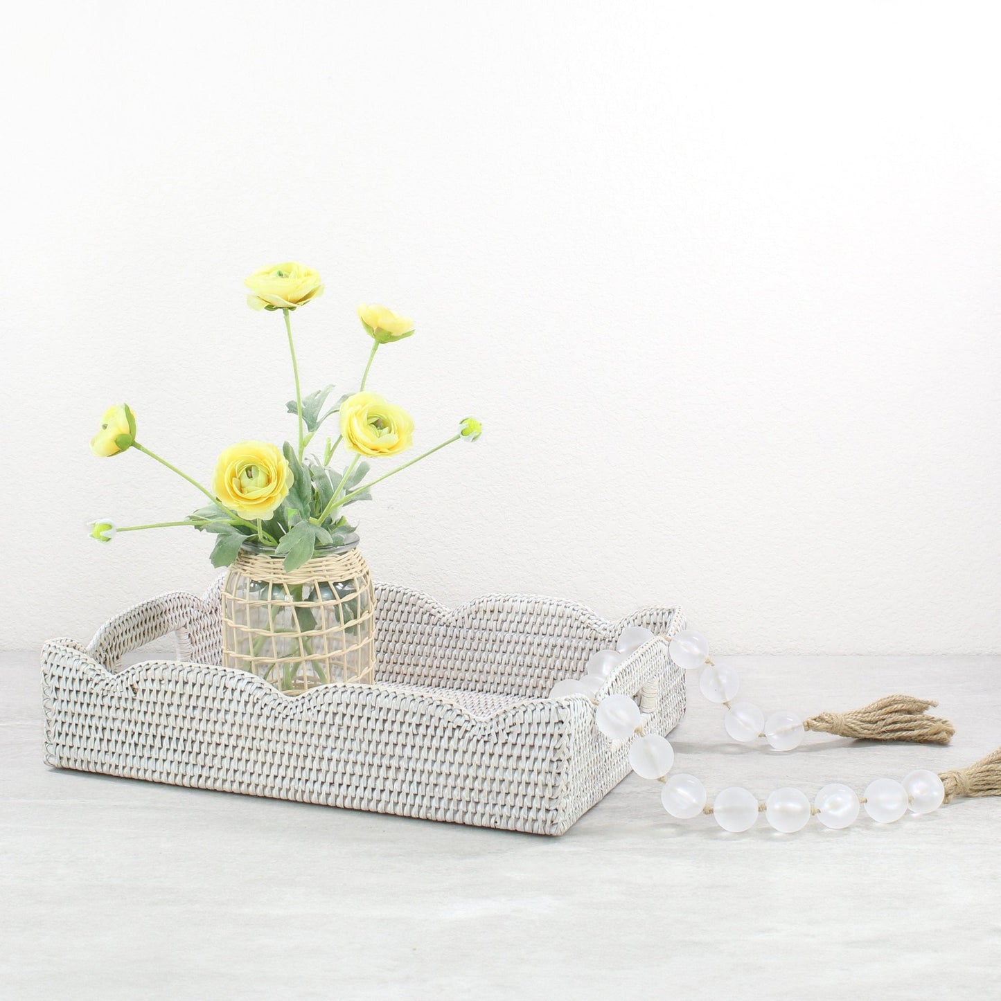 Eco Handcraft Scalloped rattan tray with vase of yellow flowers and clear bead garland on a soft gray background