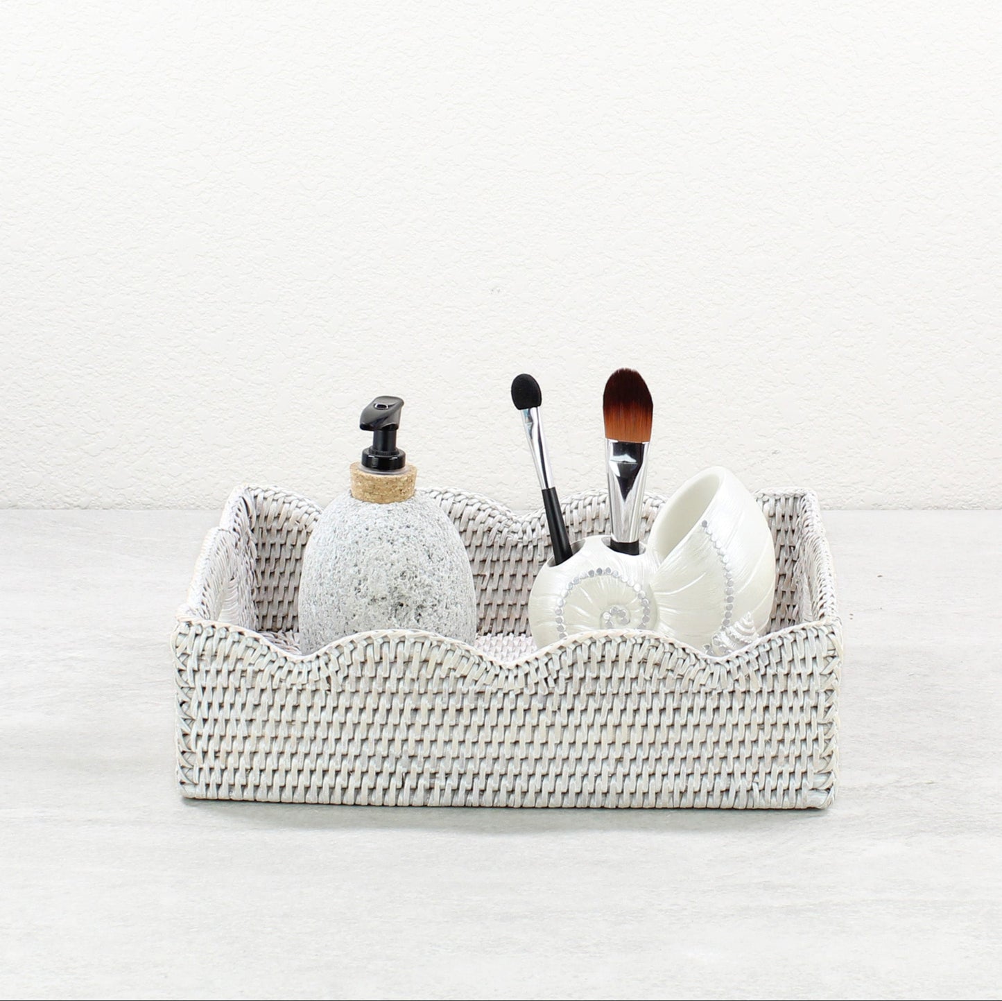 Small scalloped whitewash rattan tray holding soap dispenser and makeup brushes for stylish bathroom vanity organization