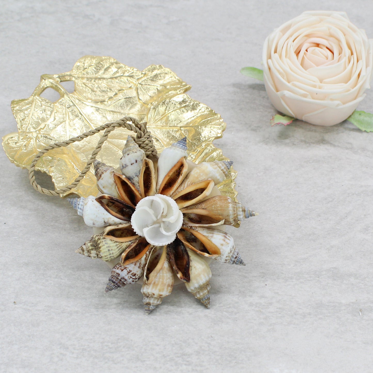 Eco Handcraft handmade Bali seashell Christmas tree ornament in natural conch blossom style, featuring brown and cream spiral shells with a central white flower, styled beside a gold leaf dish and blush rose décor.