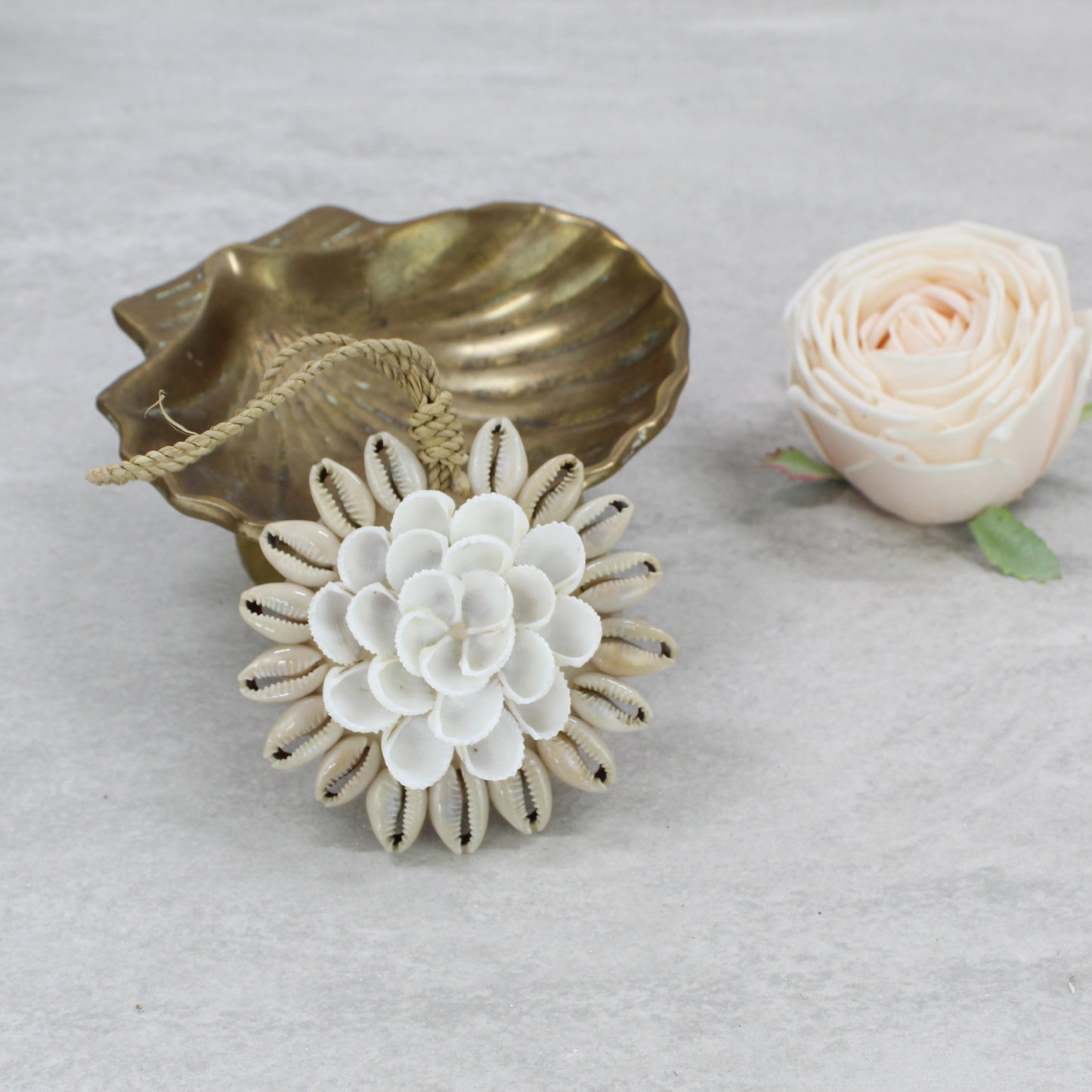 Handcrafted Bali seashell Christmas tree ornament with white cowrie and clam shells, woven raffia hanging cord, styled with gold dish background and a rose.
