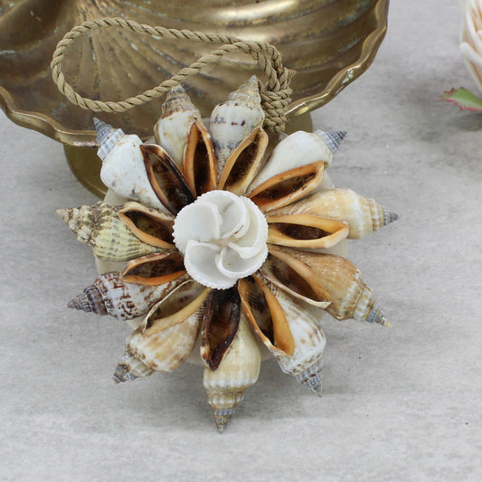 Natural Bali handmade shell Christmas bauble with spiral shells and central rose shell design, displayed beside brass bowl and soft pink flower.