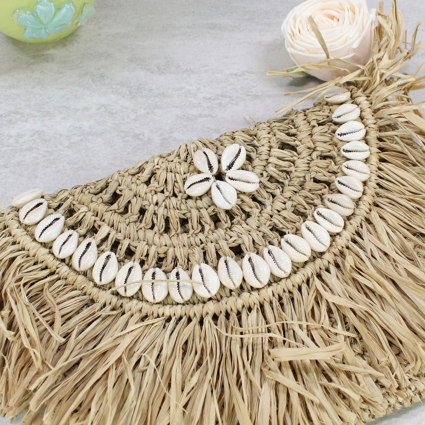 Handwoven raffia clutch with layered cowrie shell arcs and fringe -sustainable coastal fashion accessory.