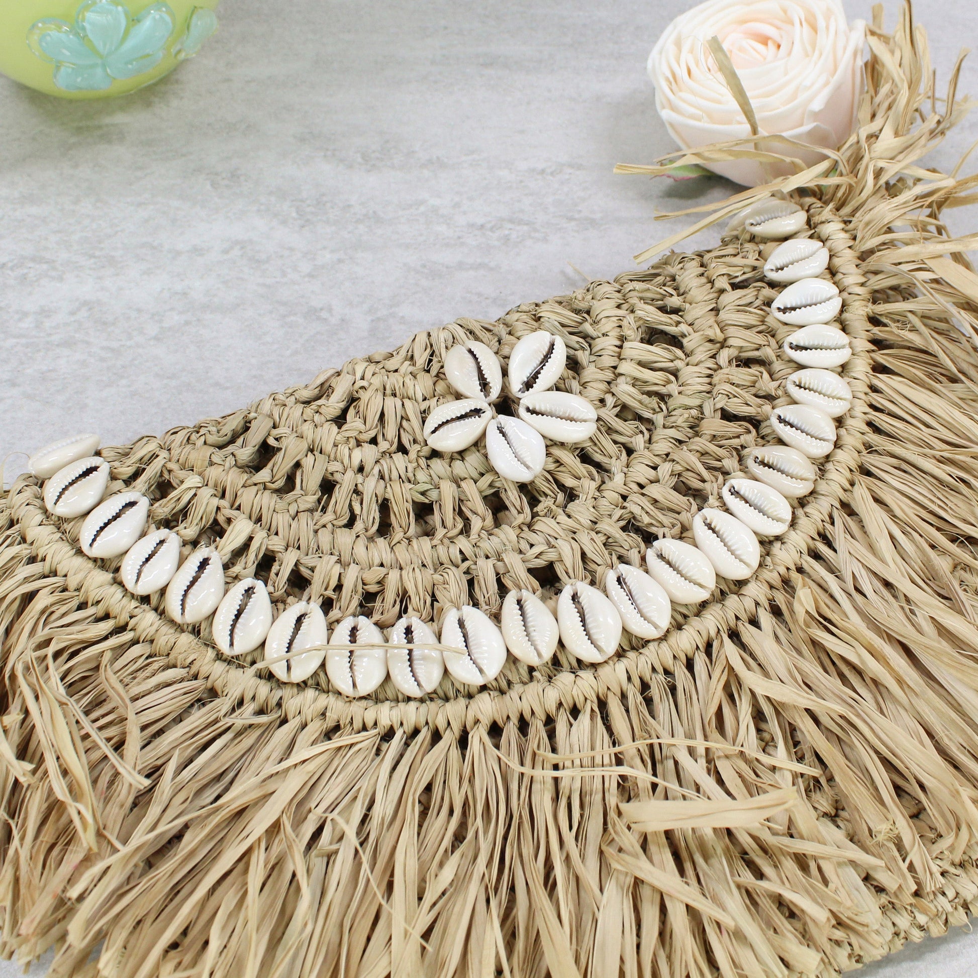 Handwoven raffia clutch with layered cowrie shell arcs and fringe -sustainable coastal fashion accessory.