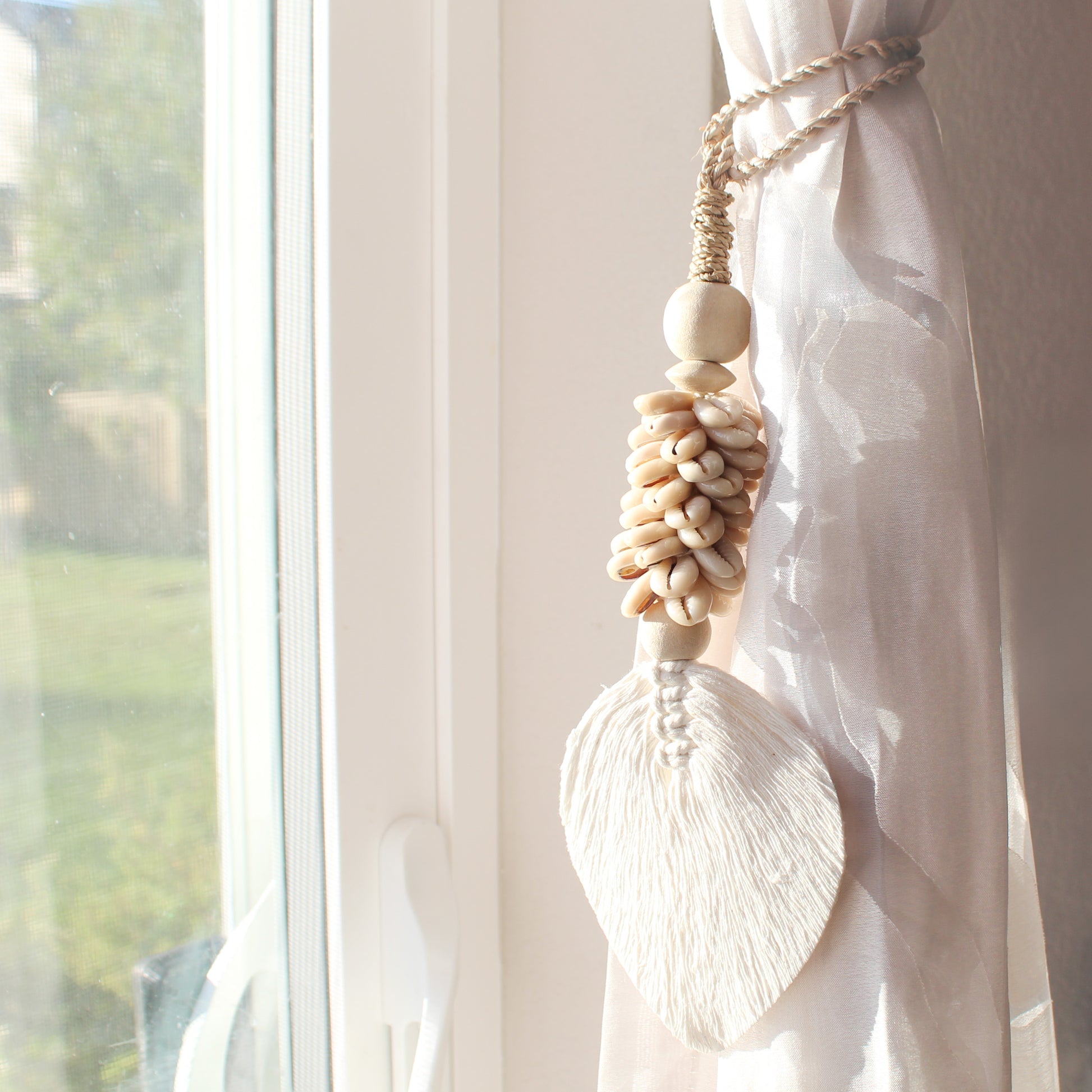 Handcrafted beige seashell tassel tied on sheer curtain near window for coastal home décor accent