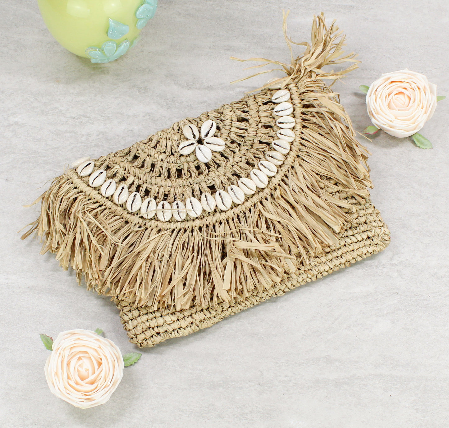 Handmade natural raffia clutch with cowrie shells and fringe on marble surface – boho summer accessory