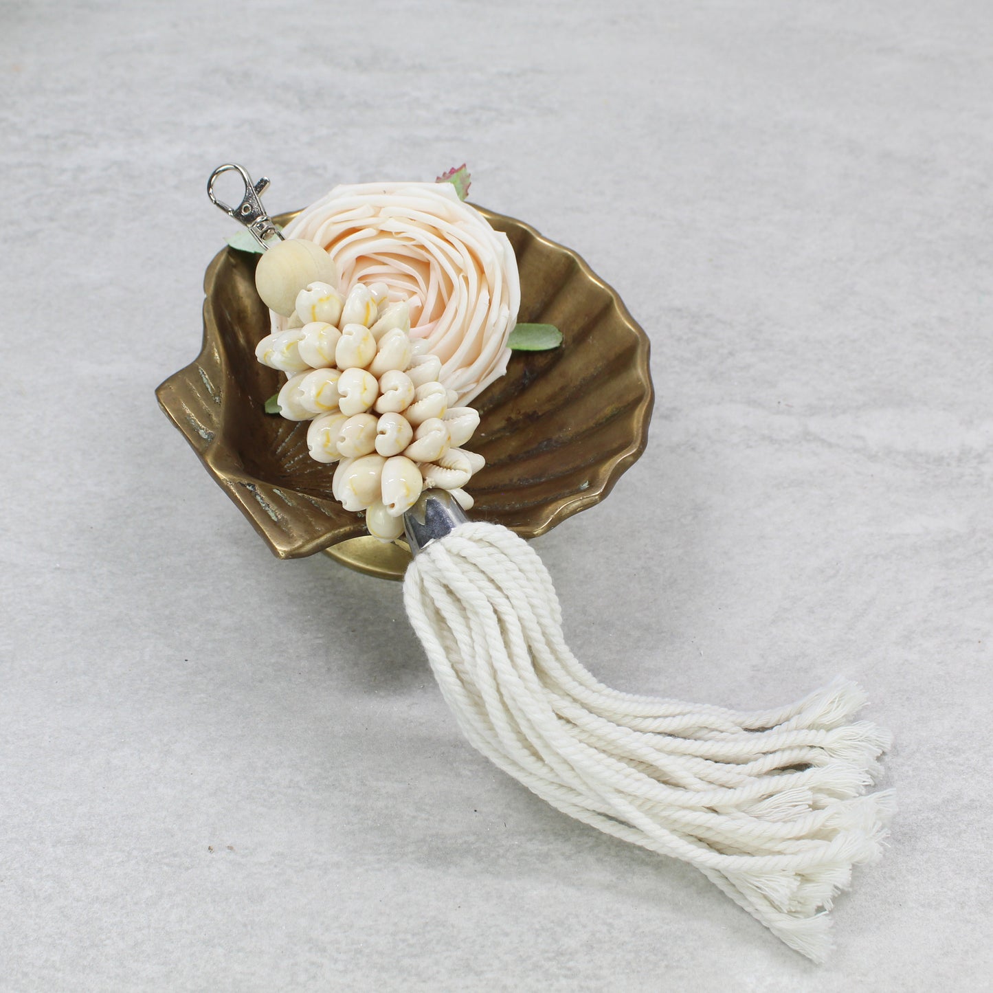Handcrafted seashell key ring with natural shells and white cotton rope tassel, displayed in elegant brass dish.