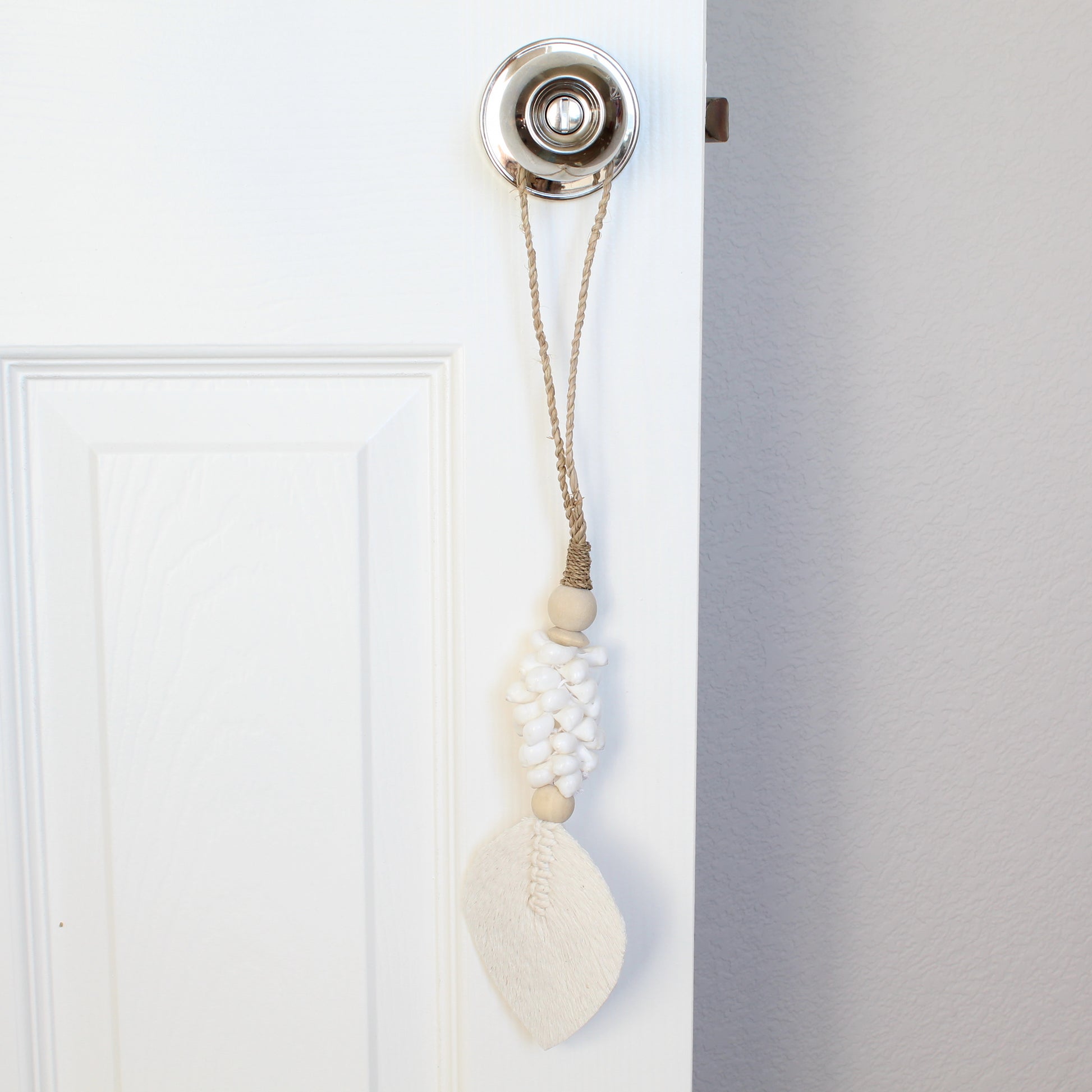 White beaded seashell tassel with braided jute loop used as boho curtain tieback on white door handle