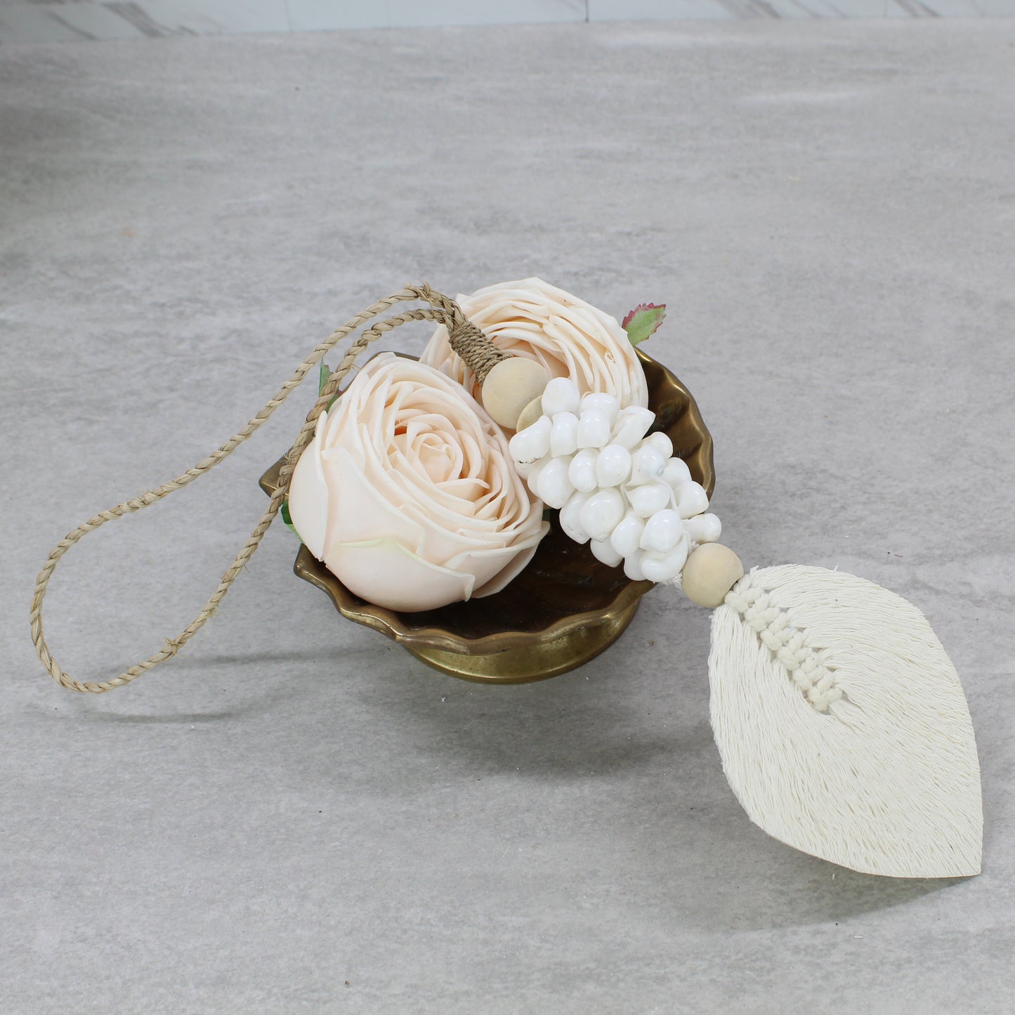 Natural white seashell tassel with macramé leaf and wood beads displayed in brass bowl with blush flowers