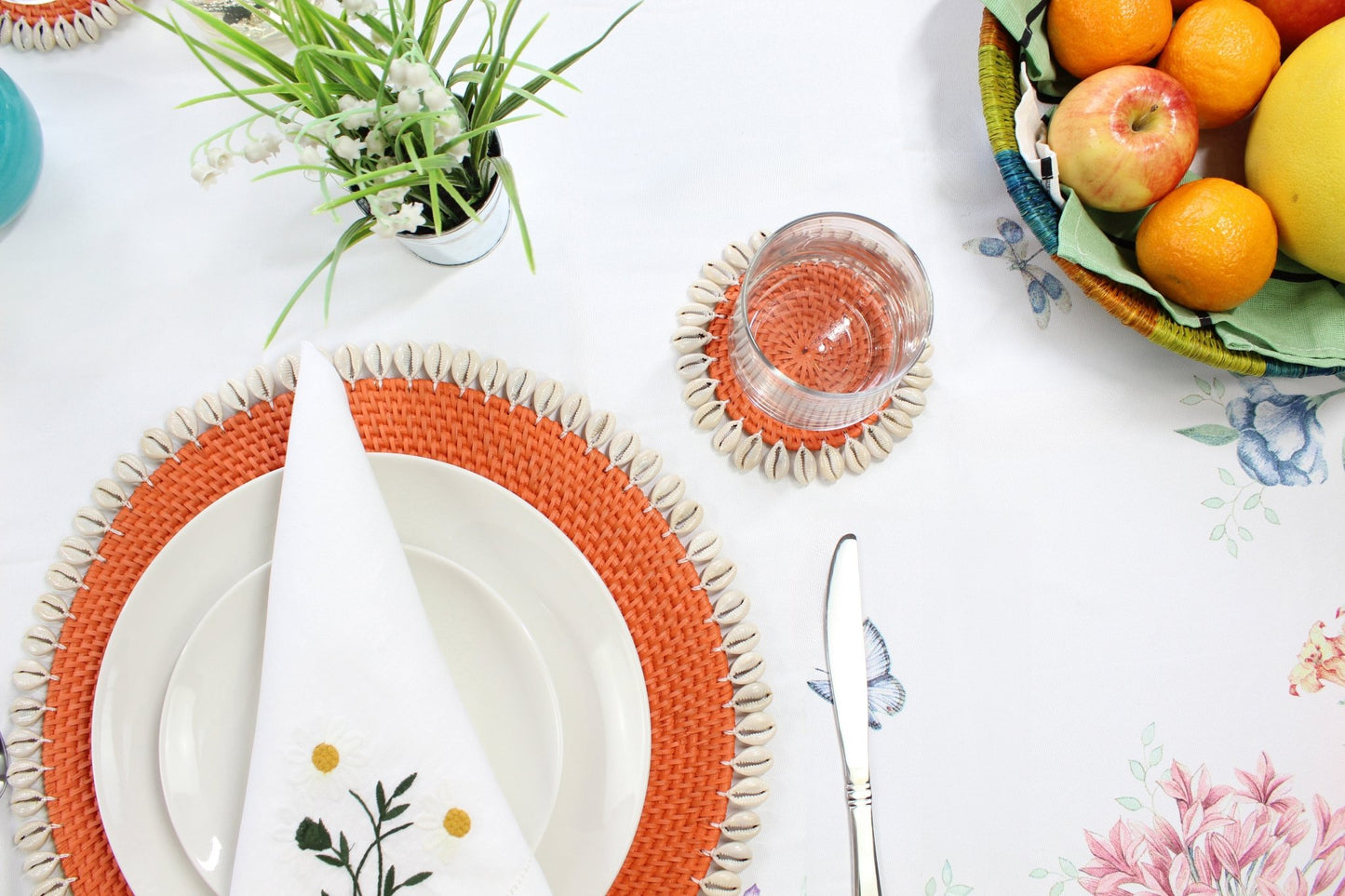 Orange eco-friendly rattan coasters styled in coastal home with candles, flowers, and tropical table décor