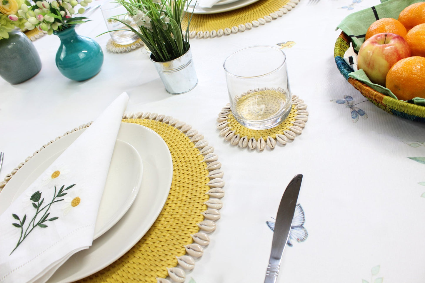 Yellow eco-friendly rattan coasters styled in coastal home with candles, flowers, and tropical table décor