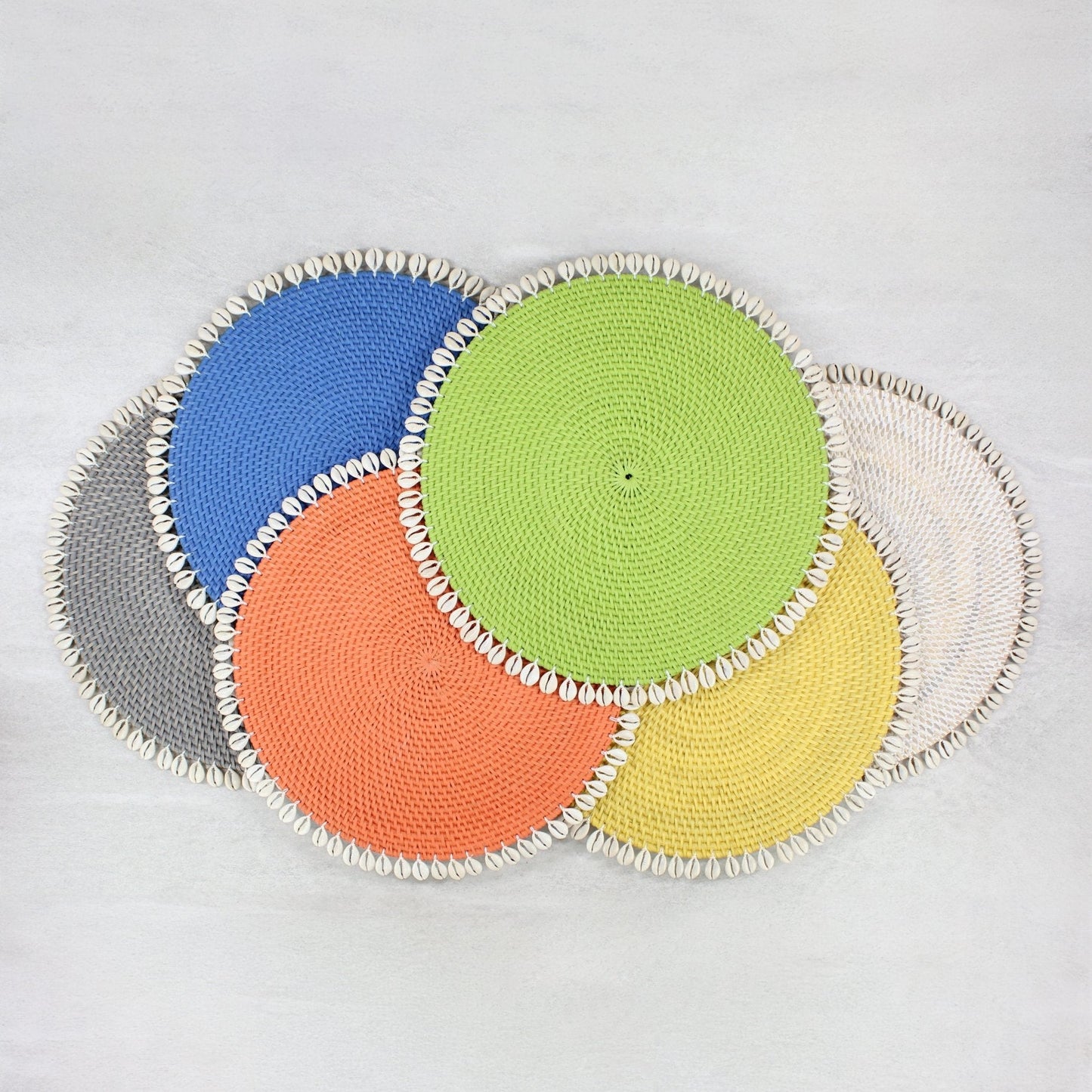 Set of colorful shell-trimmed rattan placemats in blue, gray, green, orange, yellow, and white for summer or beach dining