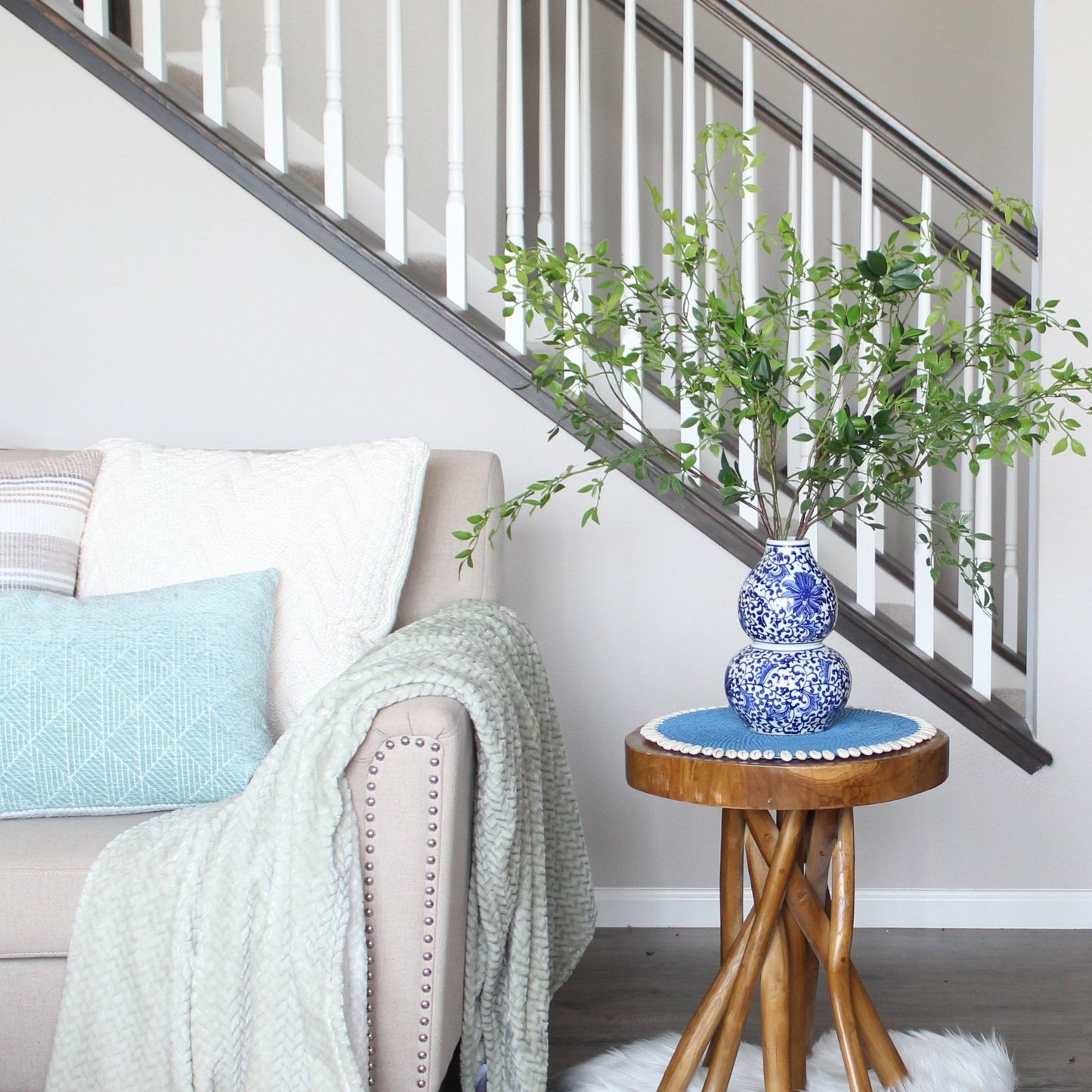 blue seashell-trimmed rattan placemat used as pad under vase, protecting tabletop and enhancing coastal presentation