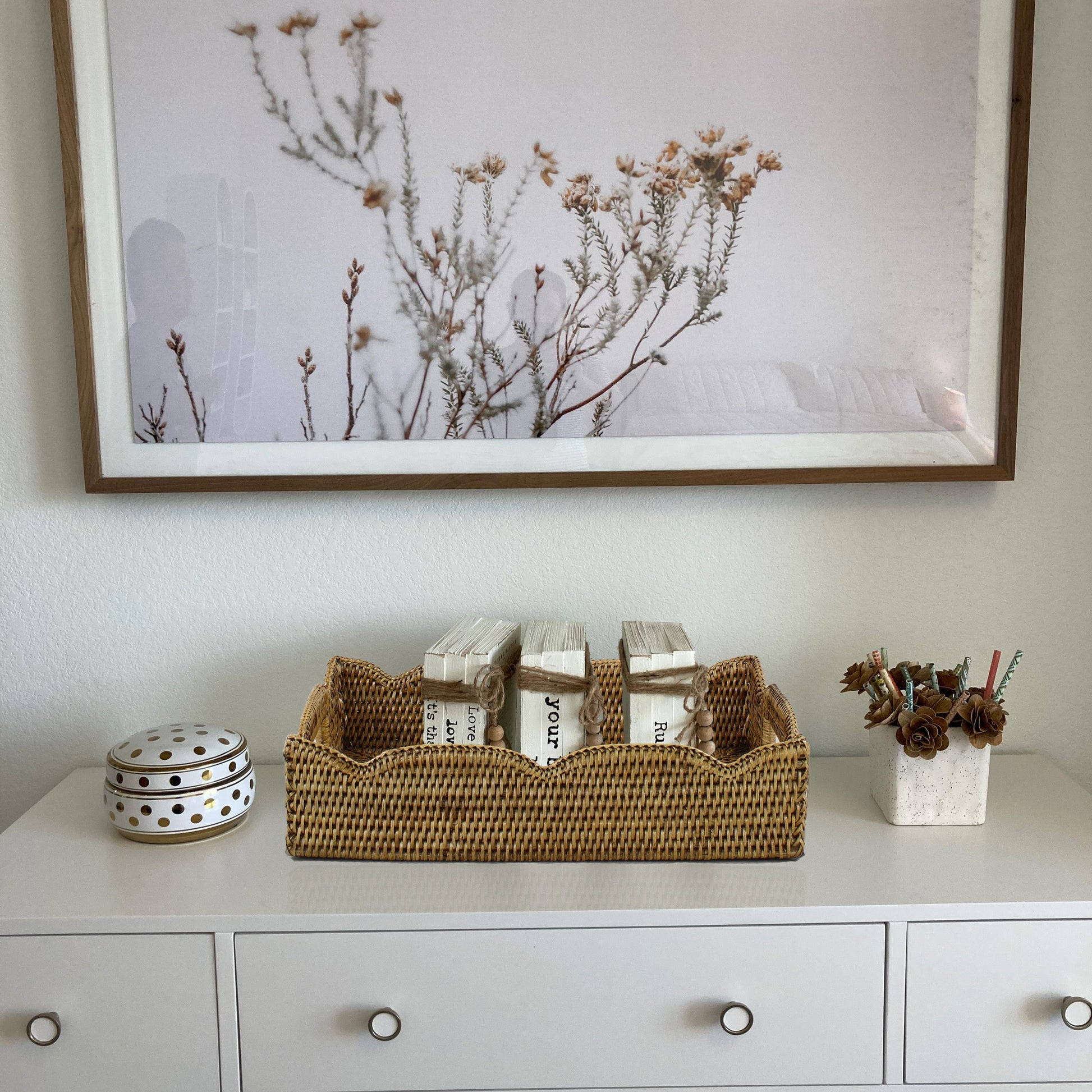 Scalloped edge rattan tray on white dresser holding rustic wrapped books, handmade eco-friendly storage and organizing décor.