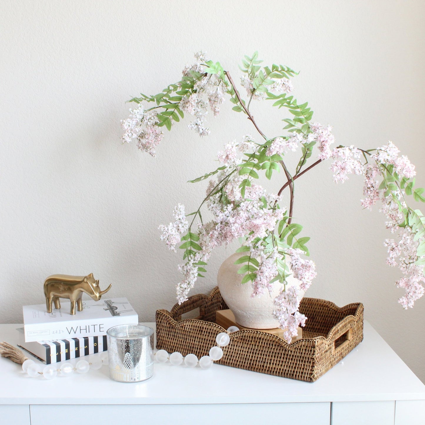 Scalloped edge honey brown rattan tray styled with neutral vase and pink floral branches, sustainable woven tray for chic home décor accents.