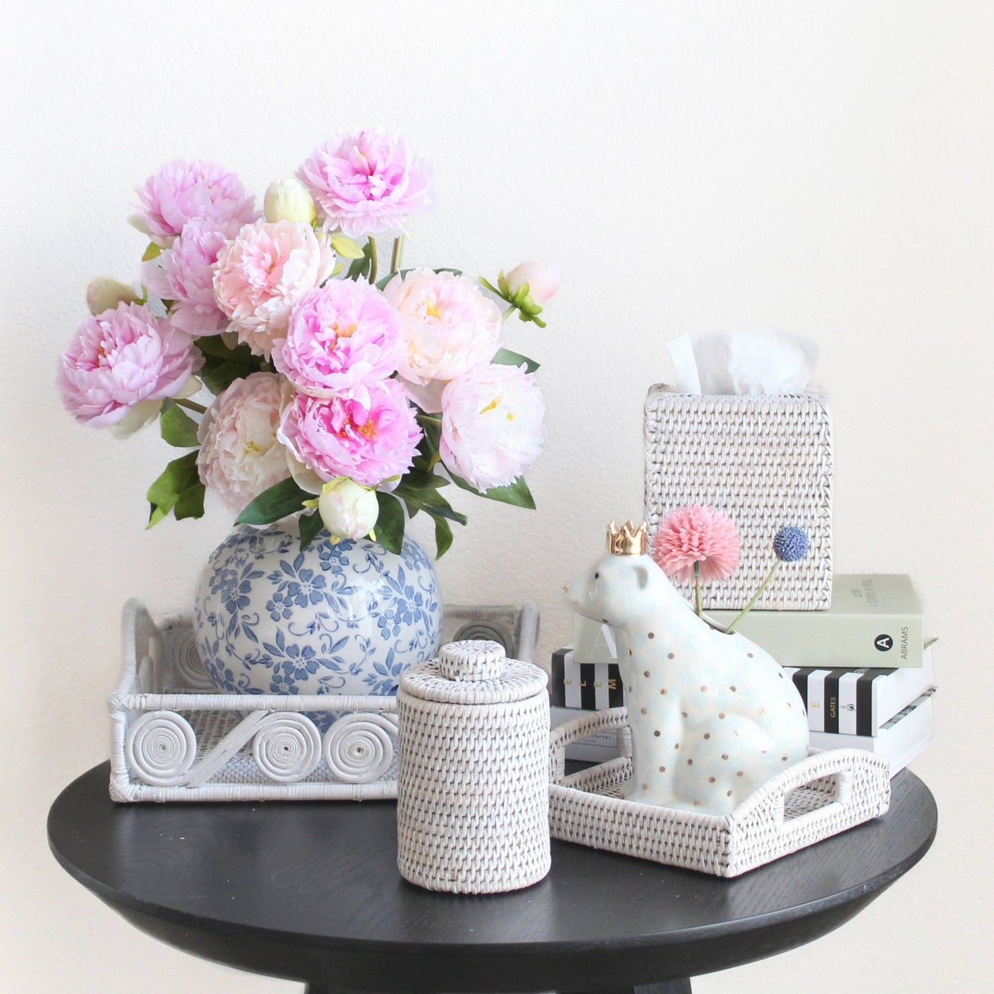 Eco Handcraft white rattan canister, trays, and tissue box styled with peonies, books, and ceramic bear on black table