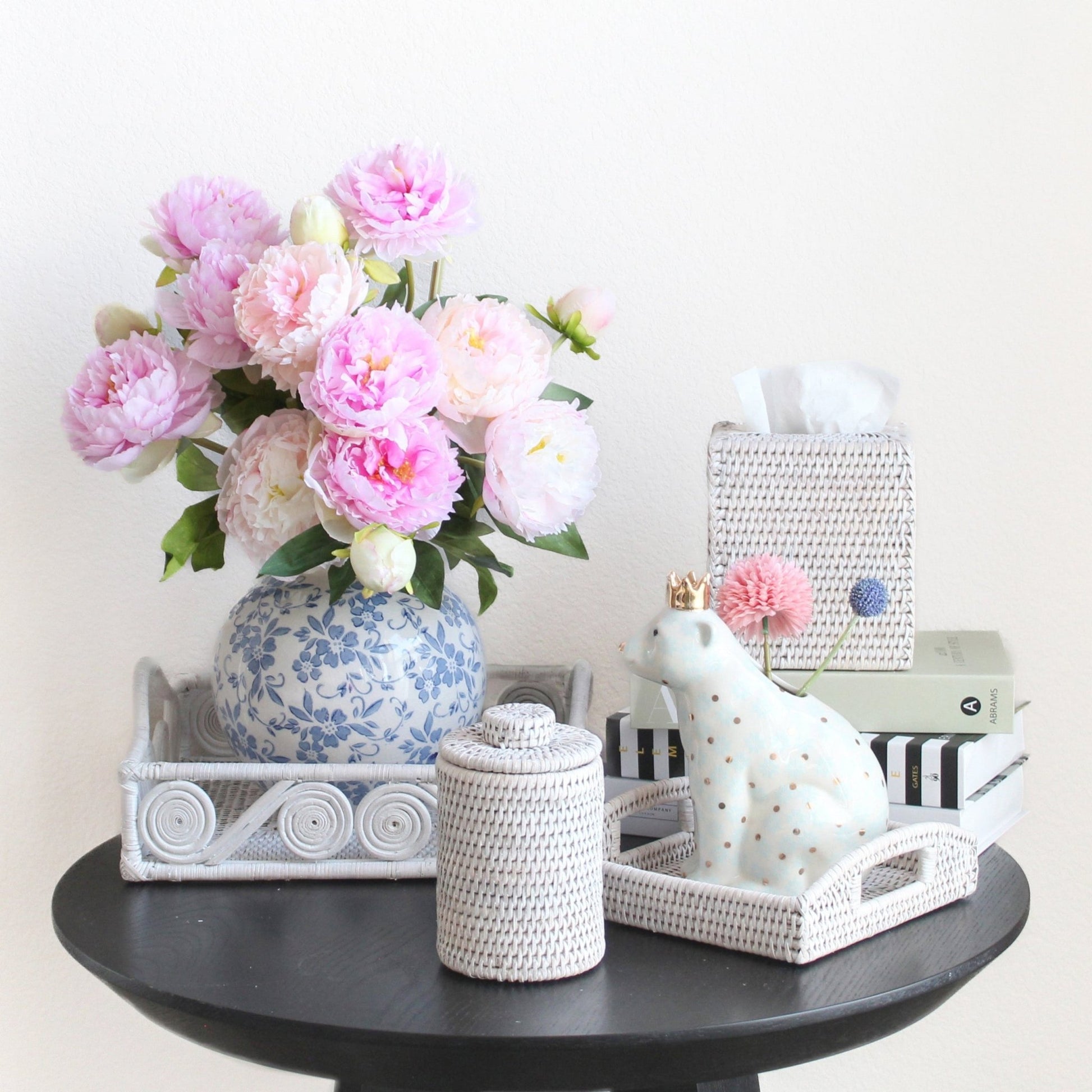 Eco Handcraft white rattan canister, trays, and tissue box styled with peonies, books, and ceramic bear on black table