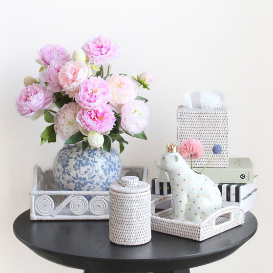 Eco Handcraft white rattan canister, trays, and tissue box styled with peonies, books, and ceramic bear on black table