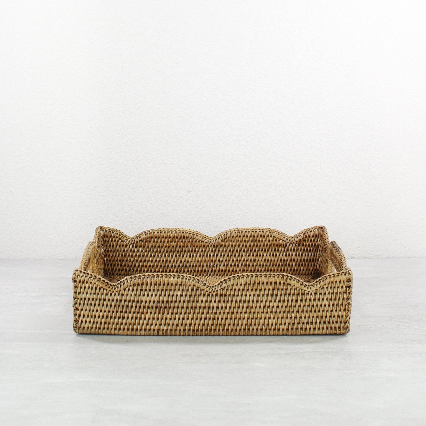 Front view of handmade scalloped rattan tray in honey brown, rectangular storage and serving basket crafted from sustainable Burmese rattan.