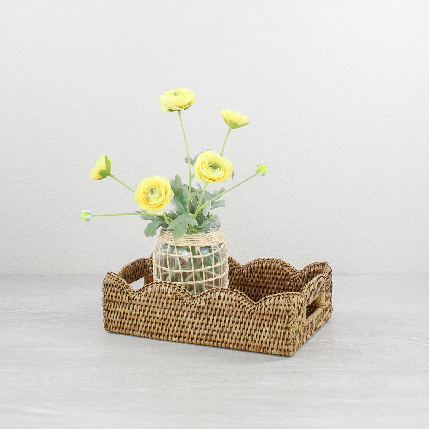 Decorative scalloped rattan tray in honey brown styled with yellow flower vase, sustainable handmade home décor accent for coffee tables or dining.
