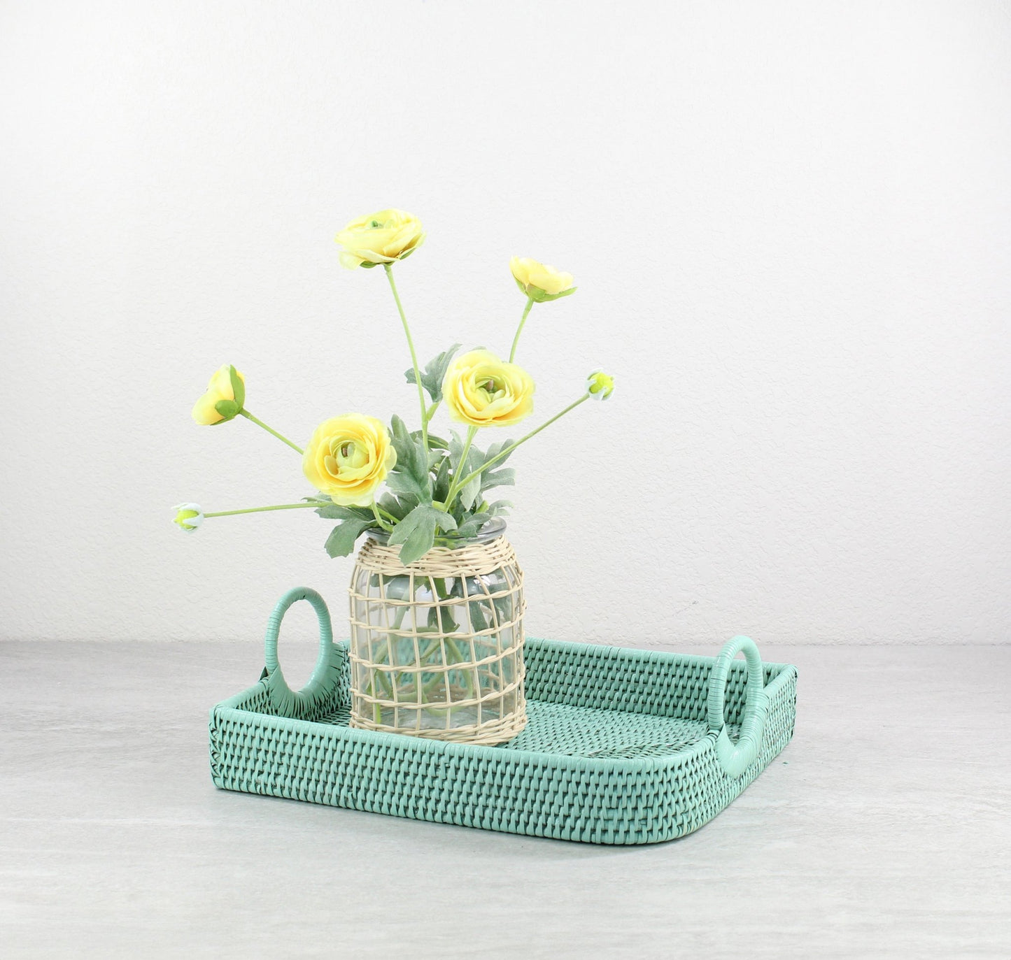 Turquoise handwoven rattan tray with a vase of yellow flowers on a light gray background