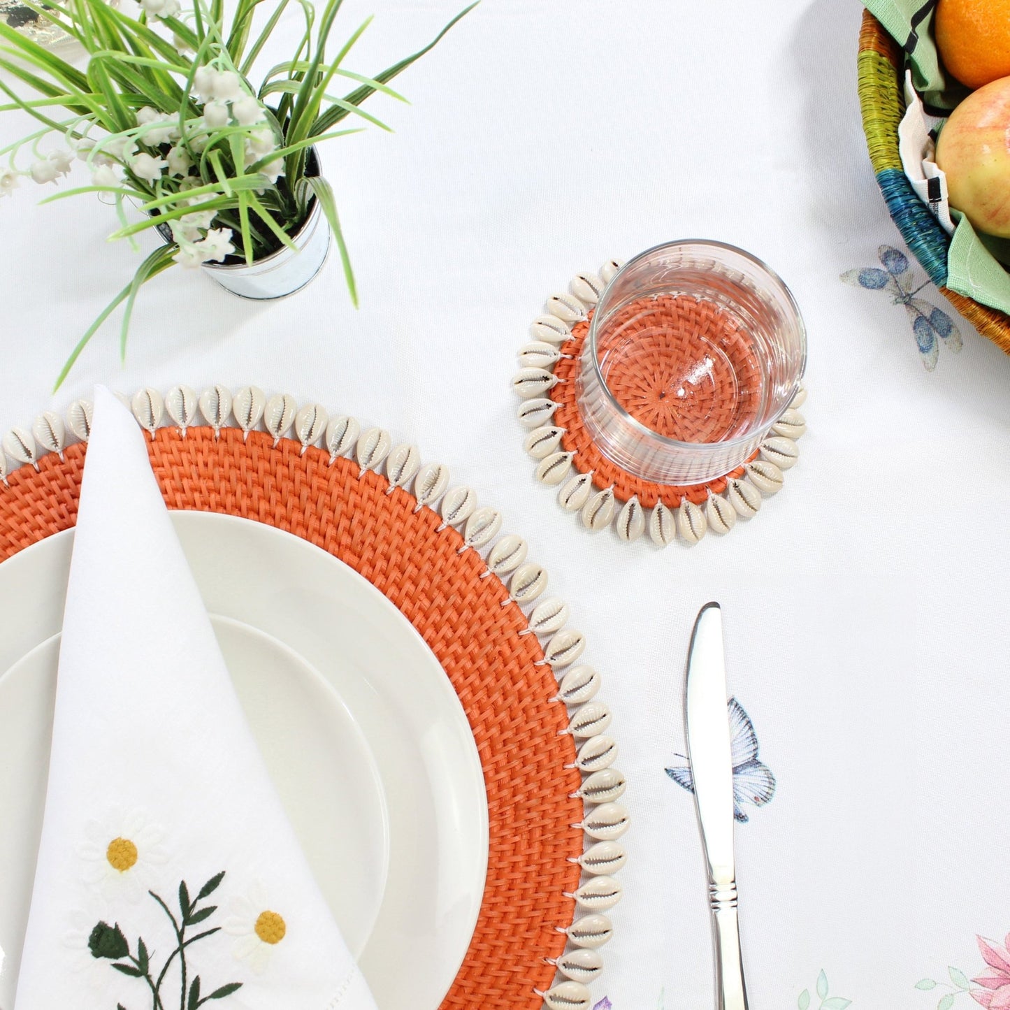 orange seashell-trimmed rattan placemat used as charger under dinnerware, protecting tabletop and enhancing coastal presentation
