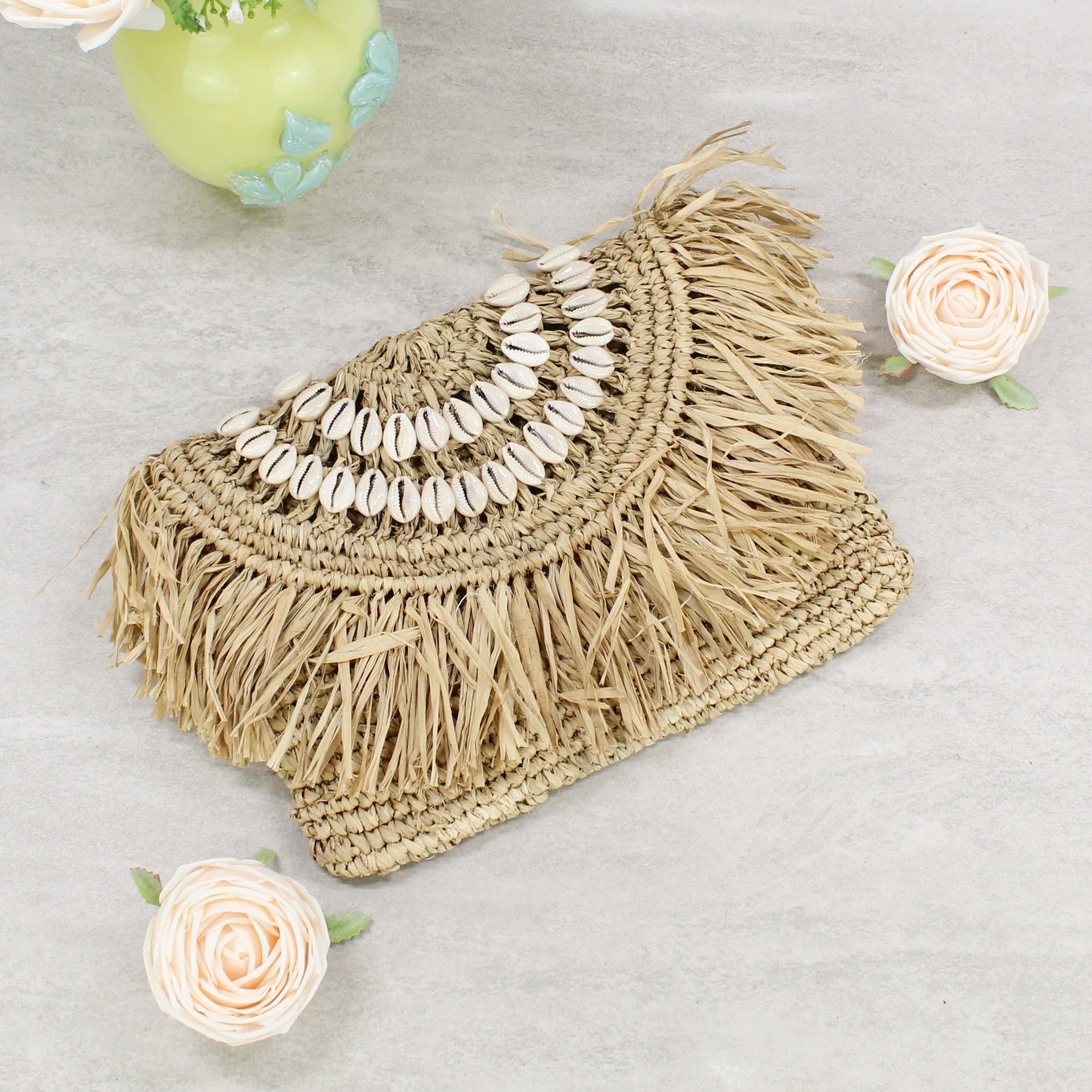 Handwoven raffia clutch with layered cowrie shell arcs and fringe - sustainable coastal fashion accessory.