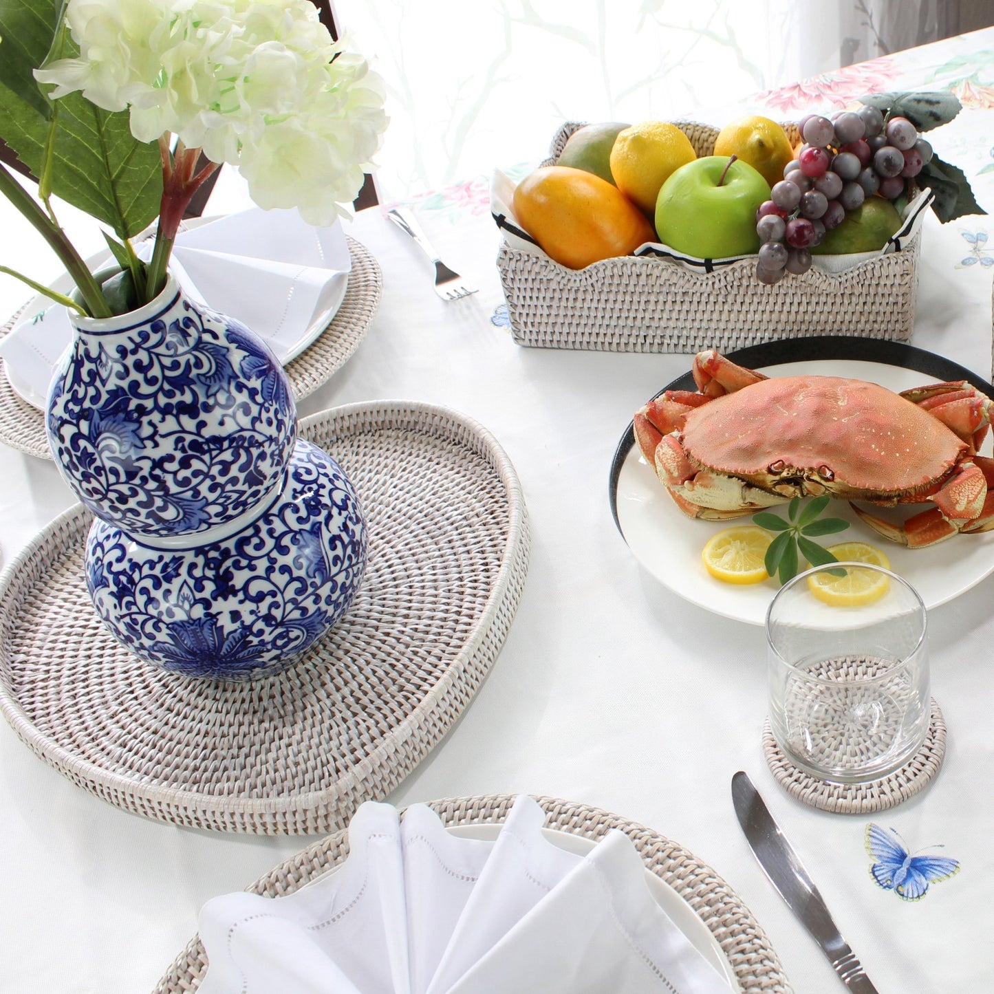 Eco Handcraft rattan trays, placemats, and coaster styled with crab dish, fruit basket, and blue vase on dining table