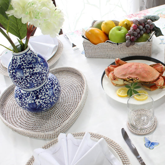 Eco Handcraft rattan trays, placemats, and coaster styled with crab dish, fruit basket, and blue vase on dining table