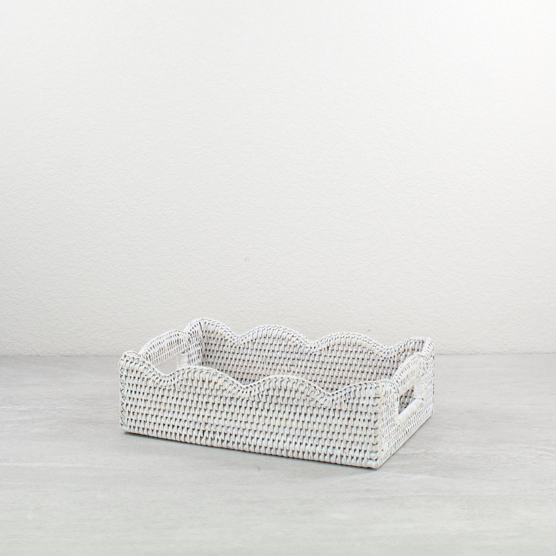 Eco Handcraft whitewash rectangle scalloped rattan tray with handles placed on a light table