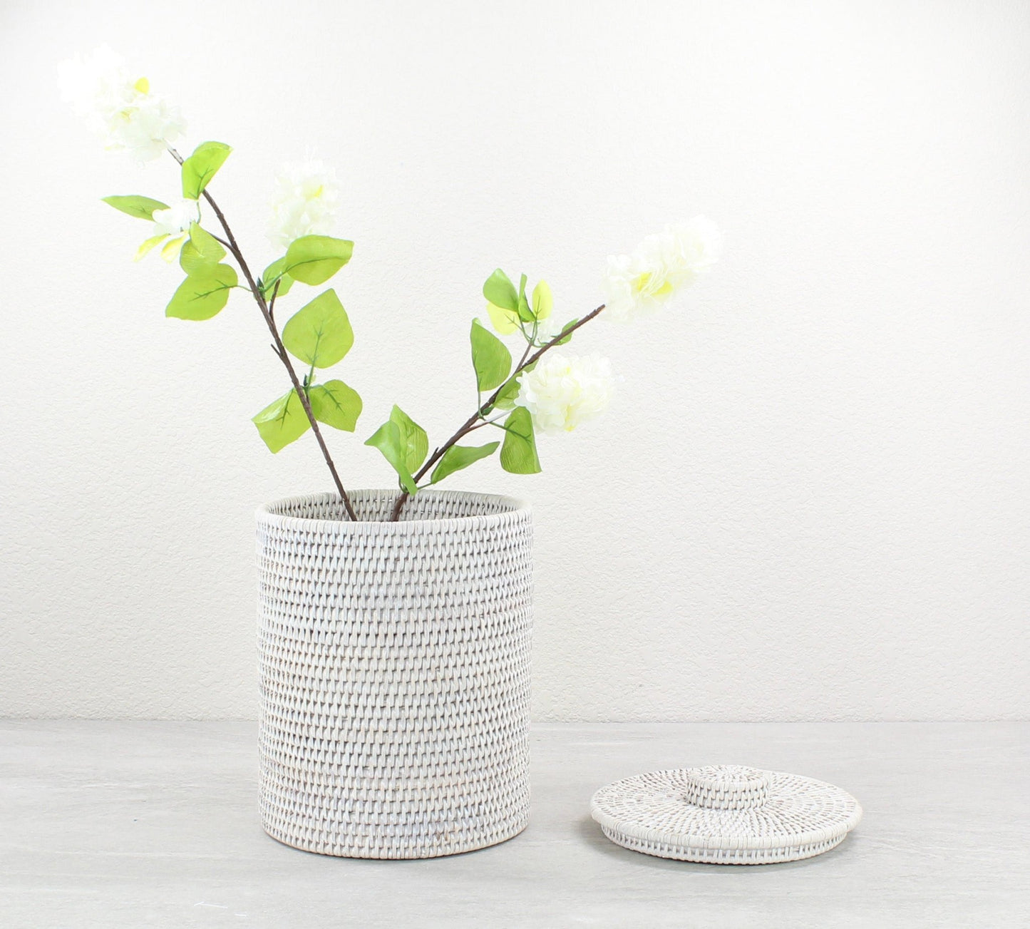 Tall white woven rattan canister with removable lid, styled with faux florals for coastal-inspired bathroom or kitchen storage