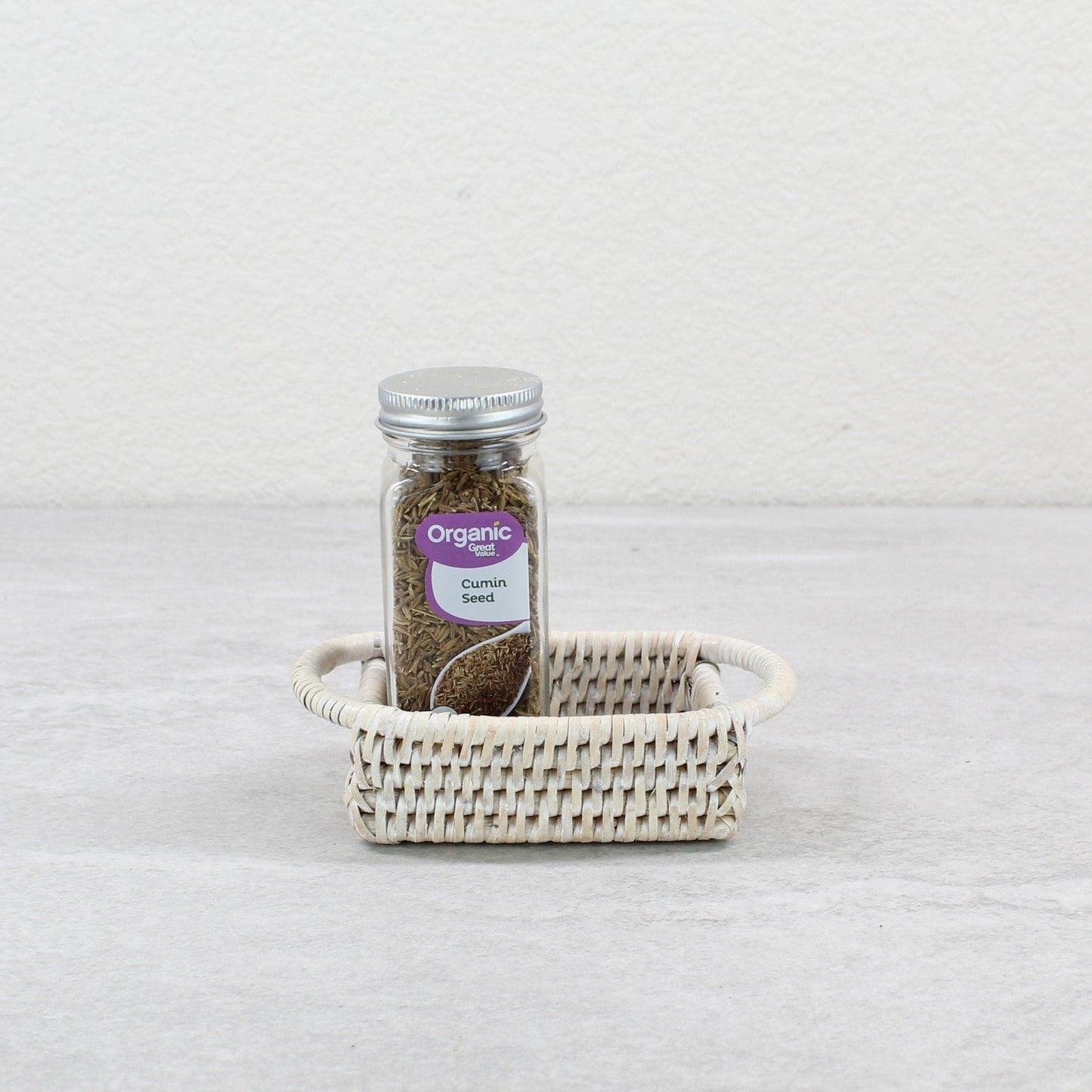 Whitewash rattan salt and pepper tray holding an organic cumin seed spice jar, styled on a light neutral background.