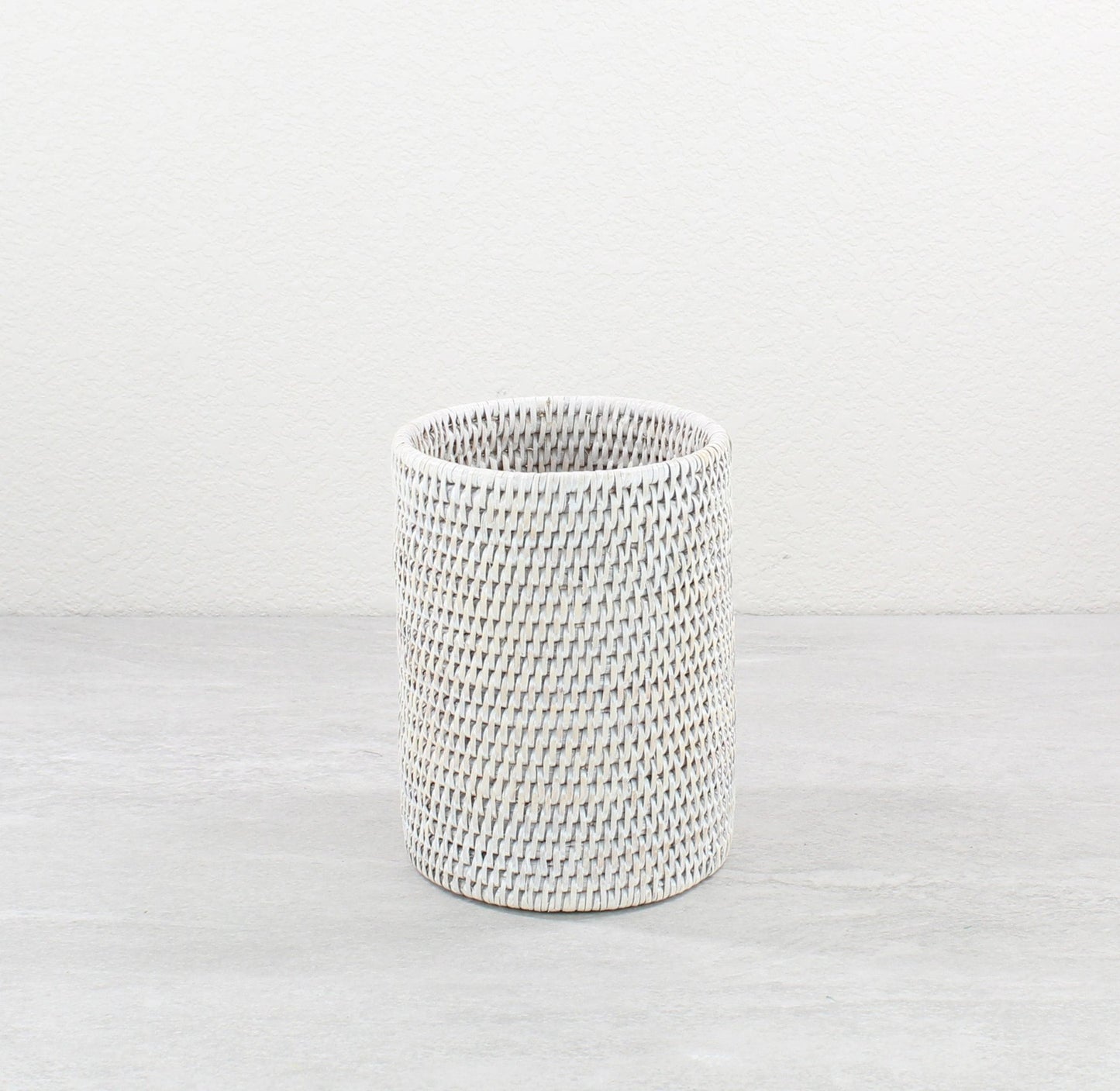 Whitewash rattan canister with tight weaving, placed on a neutral-toned surface.