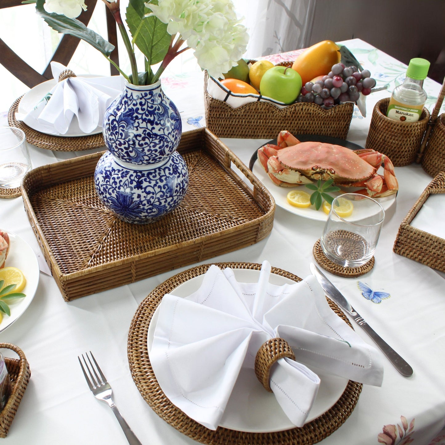 ECO HANDCRAFT rattan placemat and tray set styled with white napkin, glass, crab, and fresh fruits on table